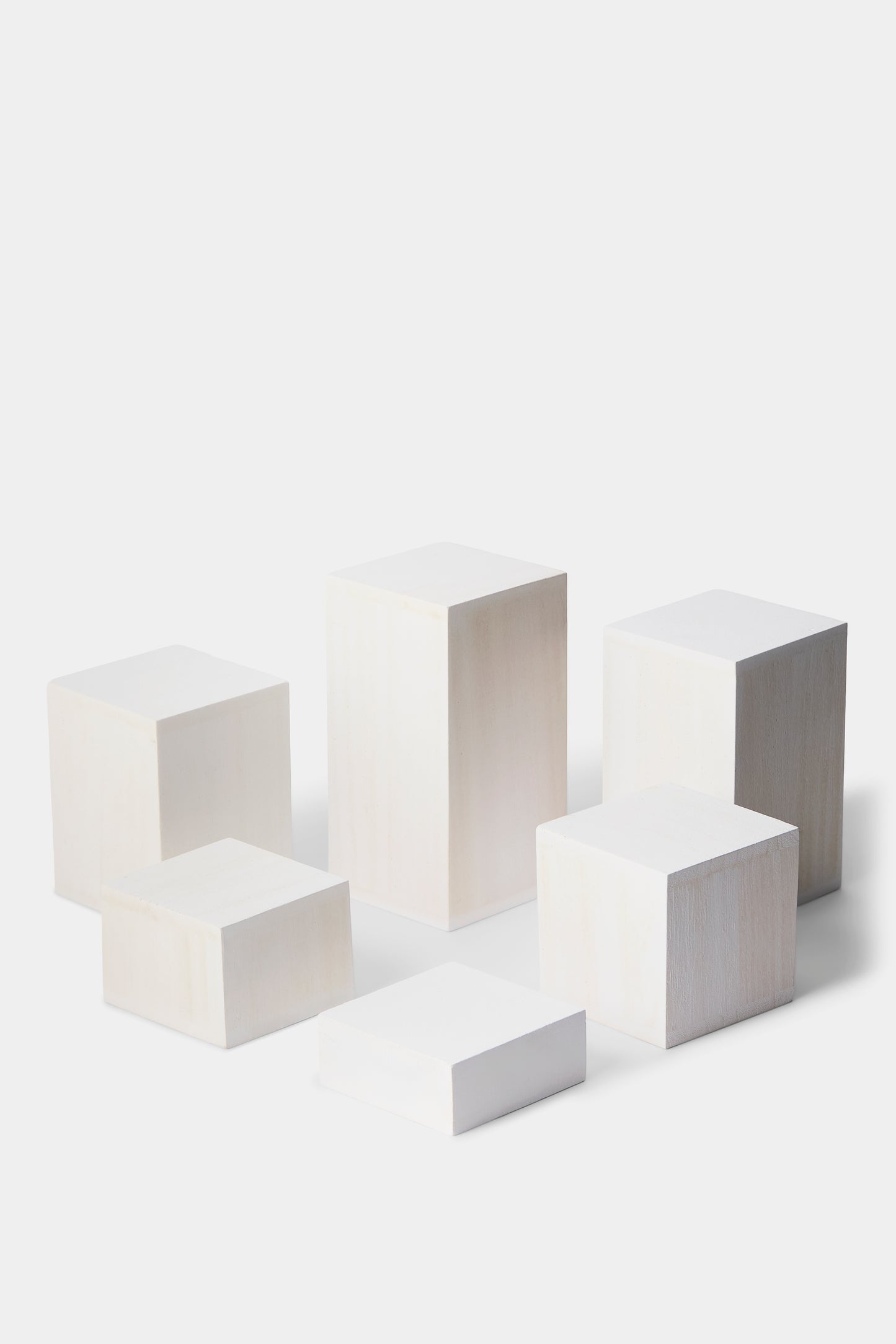 Six minimalist white rectangular display pedestals in varying heights and sizes, arranged on a seamless light gray studio background.