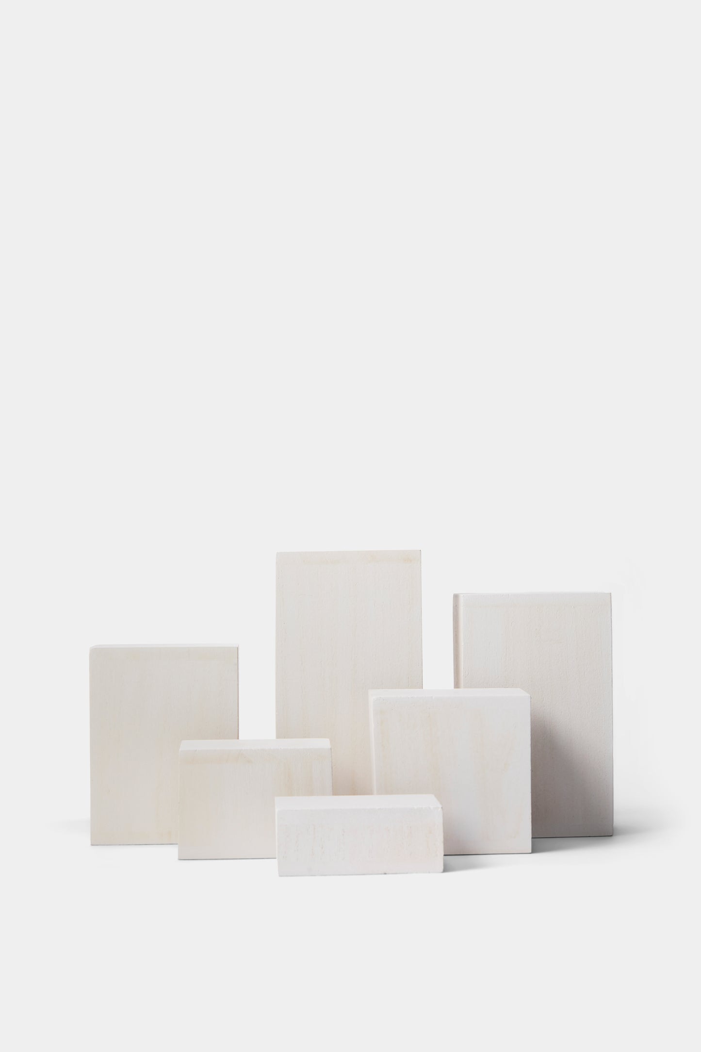 Six rectangular blocks in varying sizes, made of a light cream-colored stone or wood, arranged in a cluster against a solid white background.