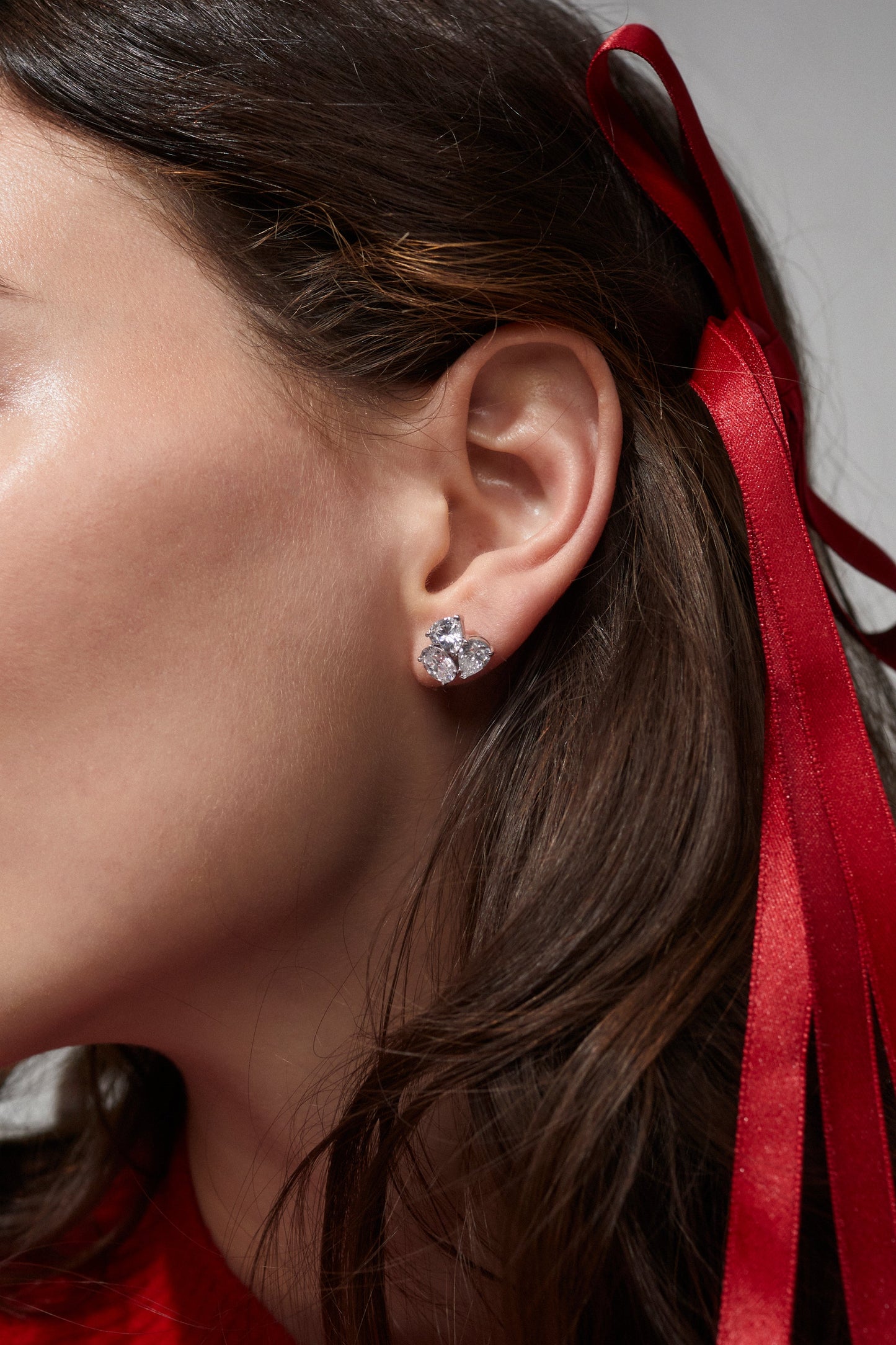REAL LOVE CZ EARRINGS ON MODEL - SIDE PROFILE VIEW OF MODEL IN A TIGHT CROP SHOT FOR DETAIL OF EARRINGS. SHE HAS A RED BOW IN HER HAIR. 