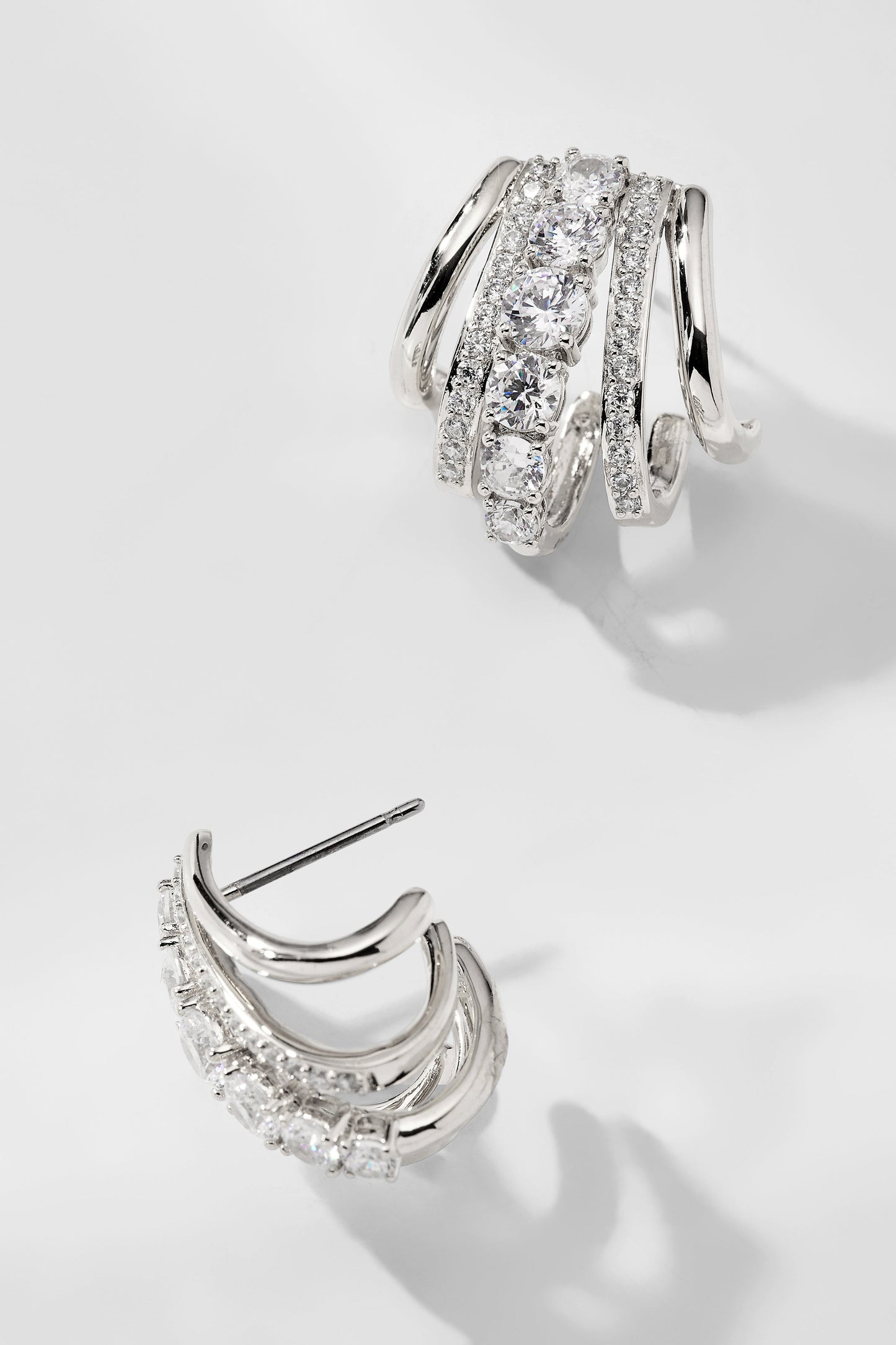 CLEO J HOOP CZ HUGGIE EARRINGS IN RHODIUM PLATING WITH ONE HOOP TURNED ON ITS SIDE TO SHOW TH POST.