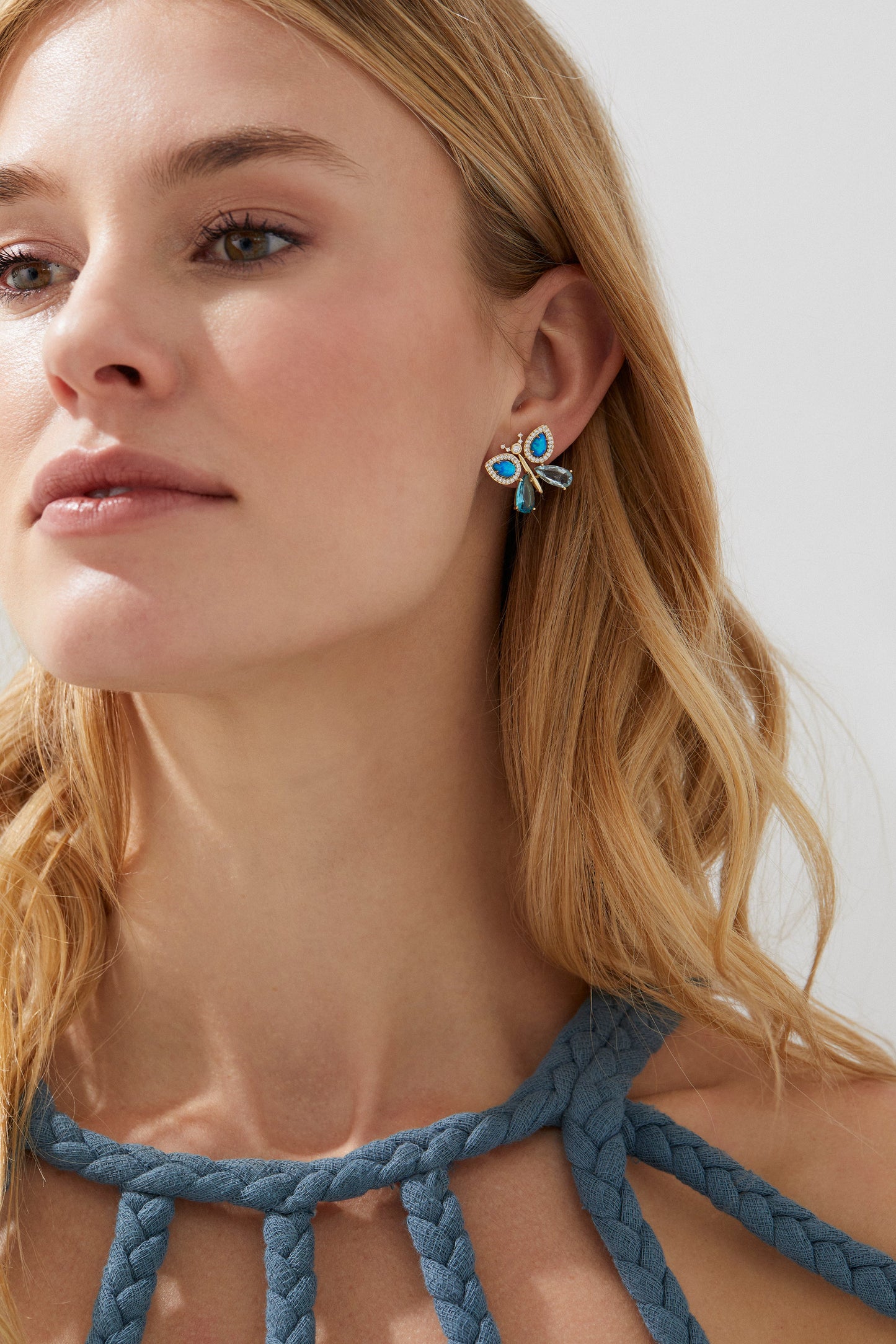BLUE LAGOON BUTTERFLY EARRINGS ON MODEL. HER BLONDE HAIR IS TUCKED BEHIND HER EARS SO THE EARRINGS ARE IN FULL VIEW. YOU CAN SEE THE TOP OF HER BLUE ROPED DRESS. 