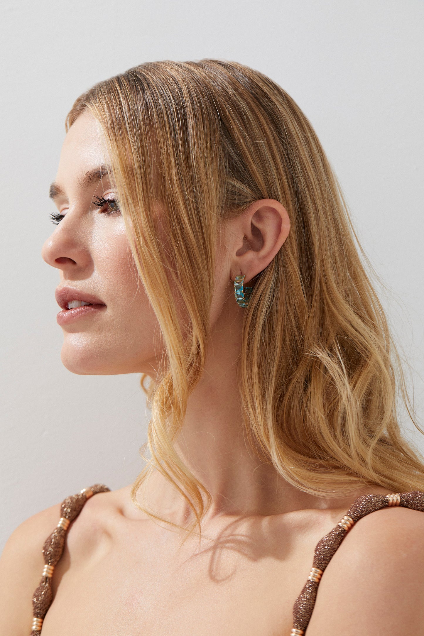 ON MODEL IMAGE OF BLUE LAGOON OMBRE C HOOP EARRINGS. SHE IS FACING TO THE SIDE WITH HER BLONDE HAIR TUCKED BEHIND HER EARS SO THE SMALL HOOPS ARE IN CLEAR VIEW. 