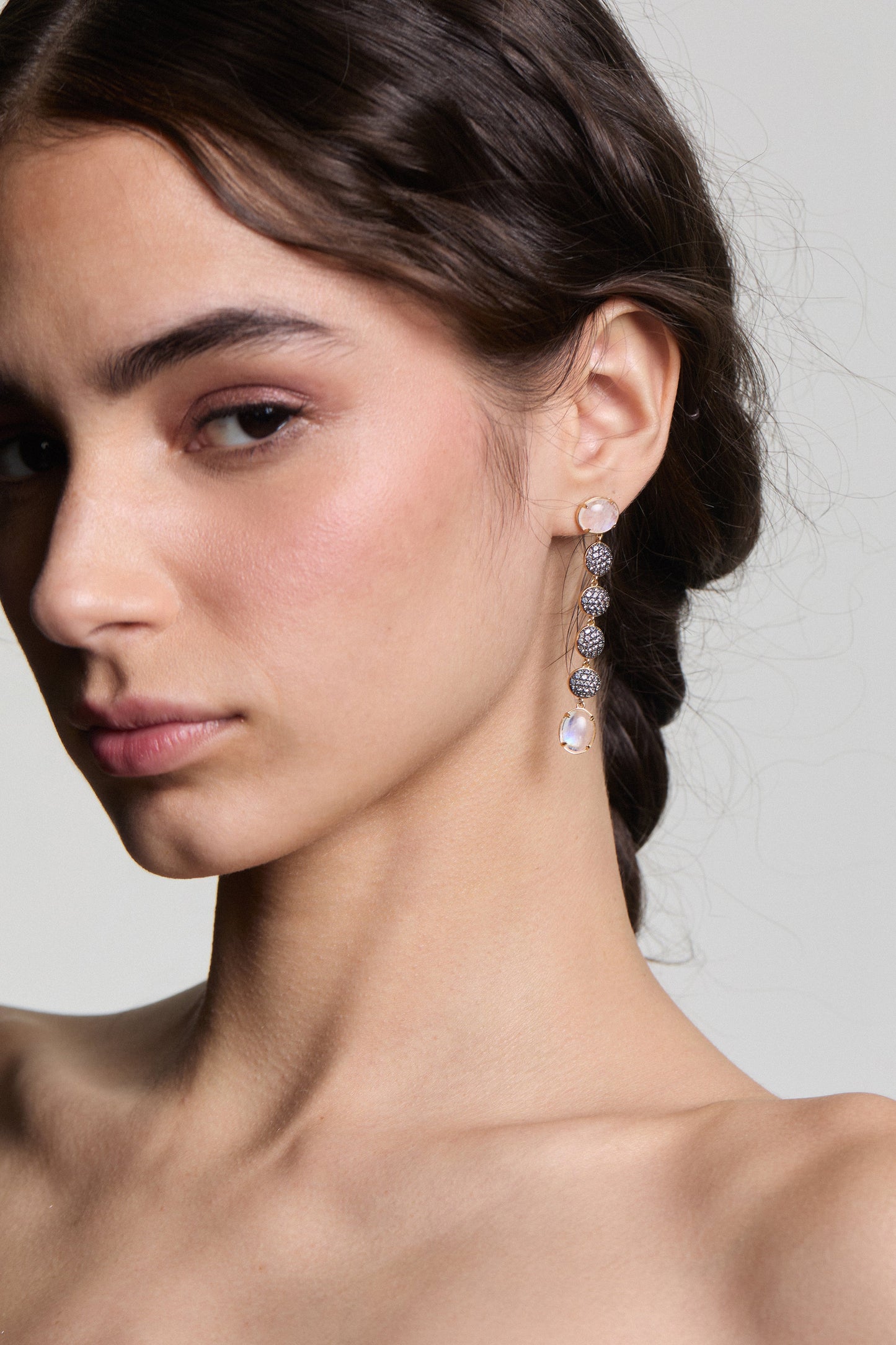 CLOSE UP OF A MODEL LOOKING AT THE CAMERA, WITH HER HAIR IN A LOOSE BRAID BEHIND HER AS SHE WEARS THE AU NATUREL LINEAR EARRINGS