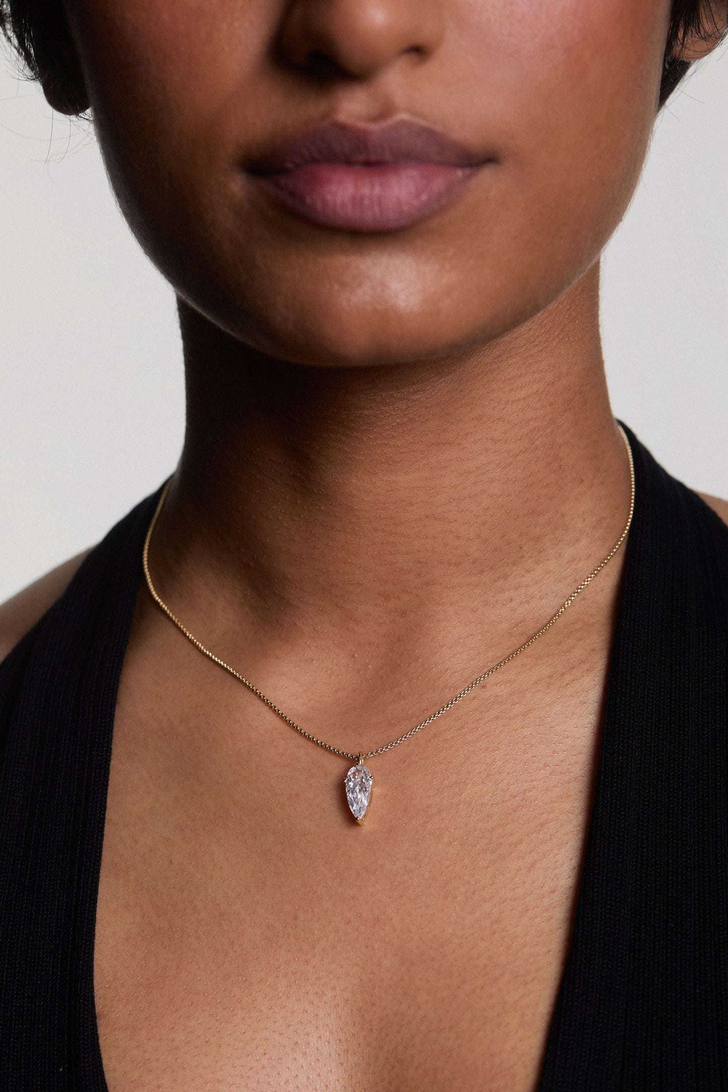 CLOSE UP OF A MODEL’S CHEST AND CHIN, HIGHLIGHTING THE LUCIA PEAR CZ PENDANT NECKLACE
