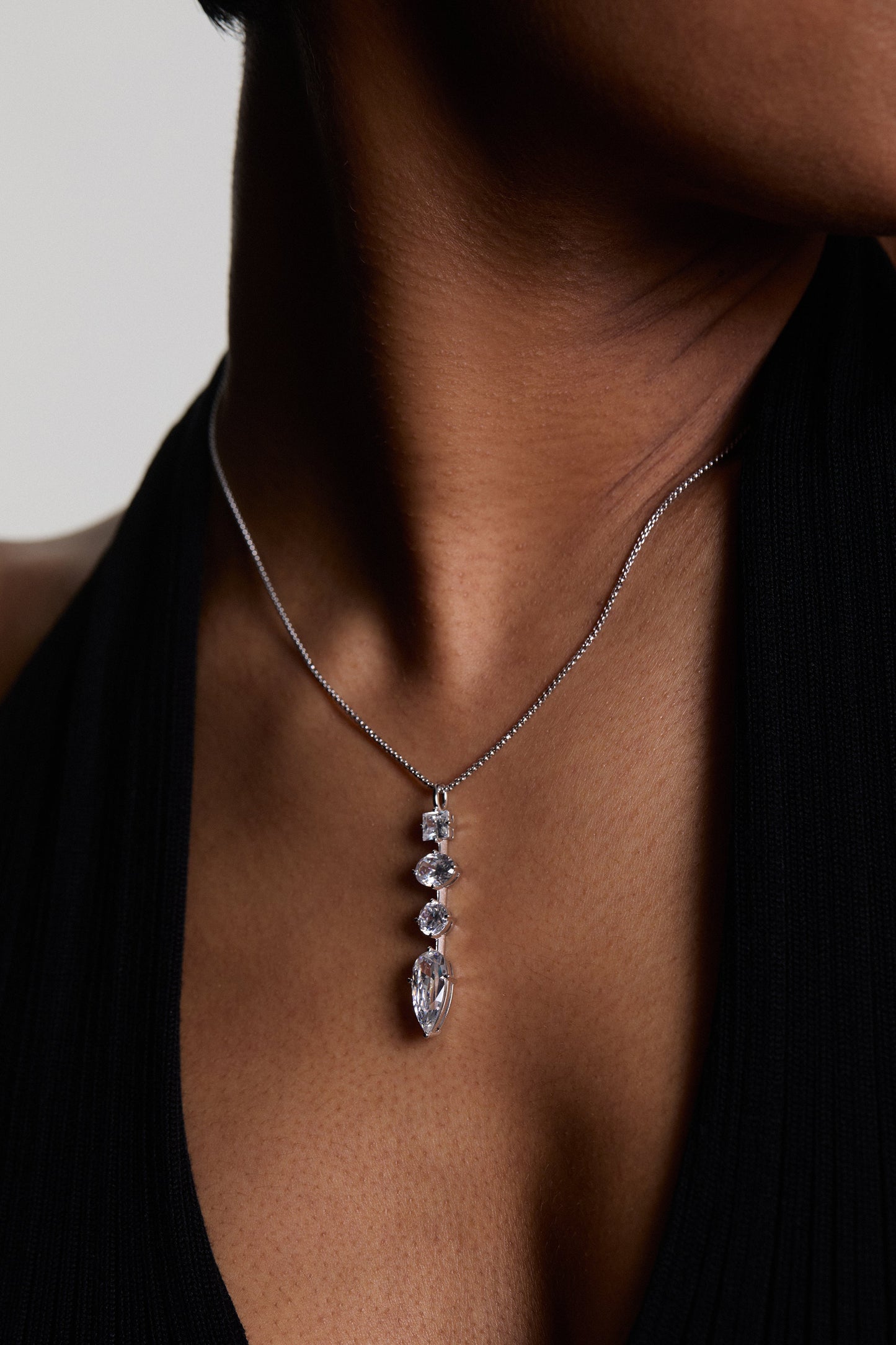 CLOSE UP OF A MODEL’S CHEST WEARING THE LUCIA LINEAR PENDANT NECKLACE, STYLED WITH A BLACK TOP