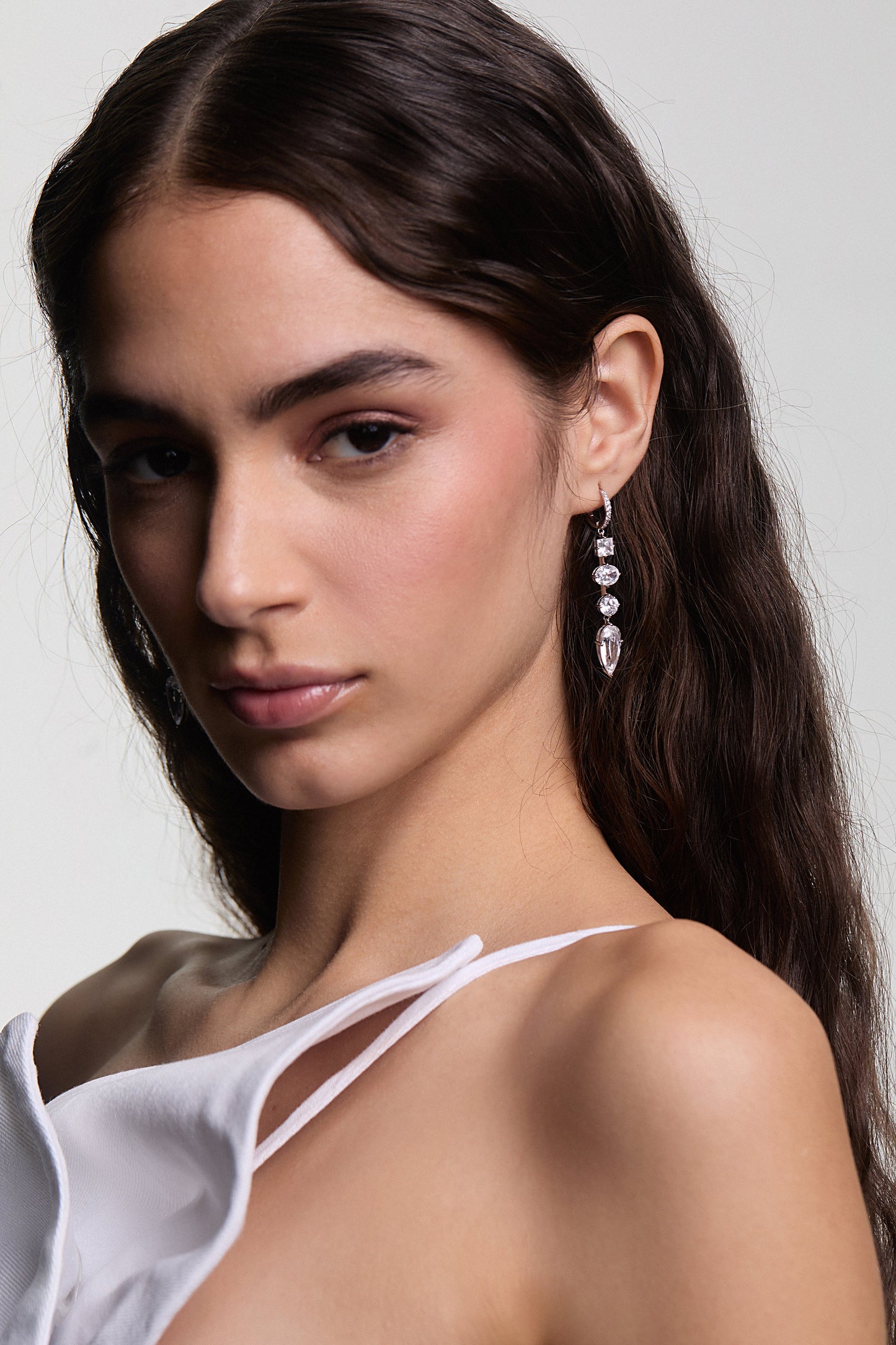 A MODEL LOOKING AT THE CAMERA WITH HER HAIR TUCKED BEHIND HER EAR WEARING LUCIA LINEAR LEVERBACK EARRINGS AND A WHITE, STRAPPY TOP