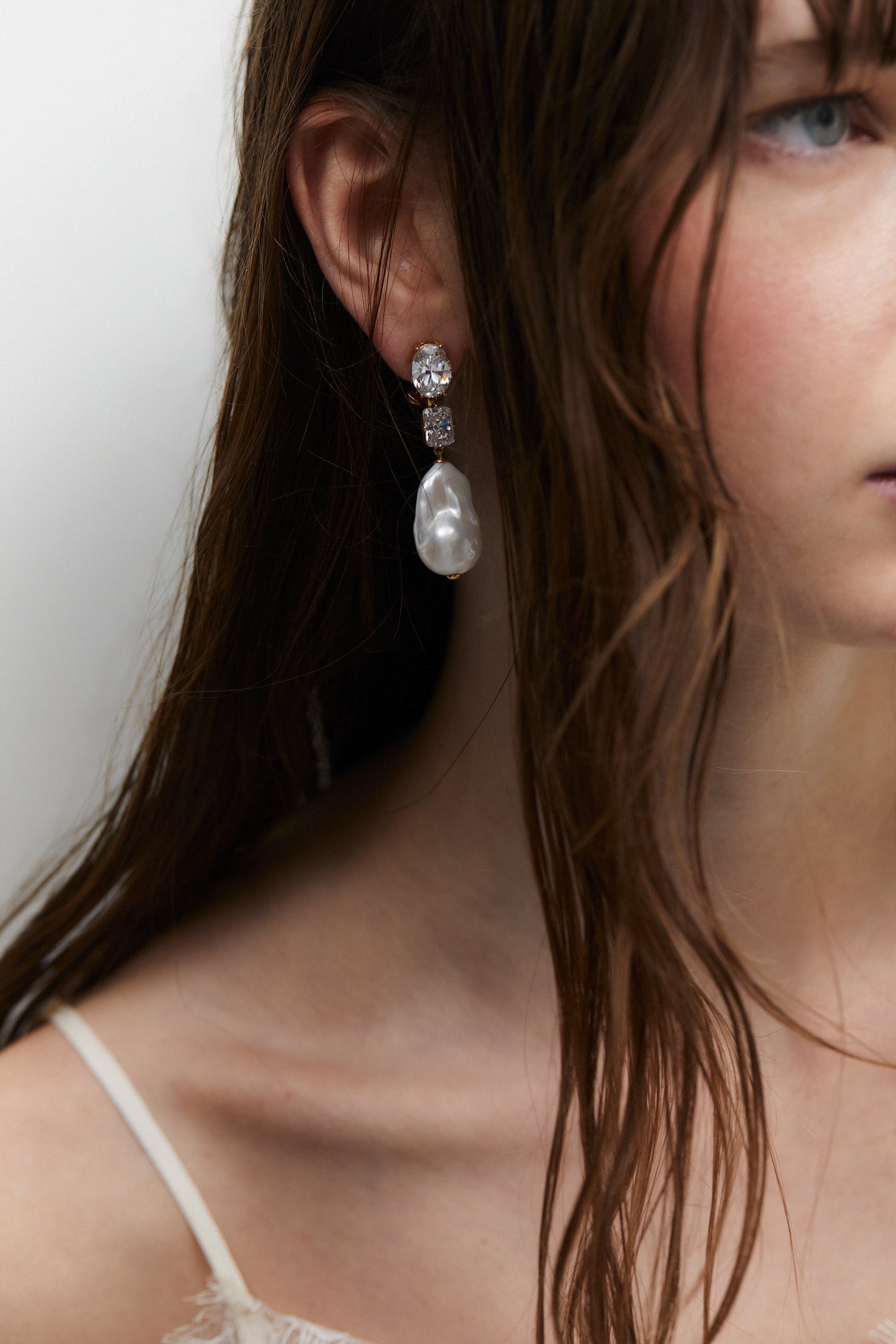 MODEL WEARING MADRID FRESHWATER PEARL TRIPLE DROP EARRINGS. IT IS A CLOSE UP IMAGE OF HER EAR WITH HALF HER FACE CROPED OUT AND HAIR BEHIND THE SHOULDER. 