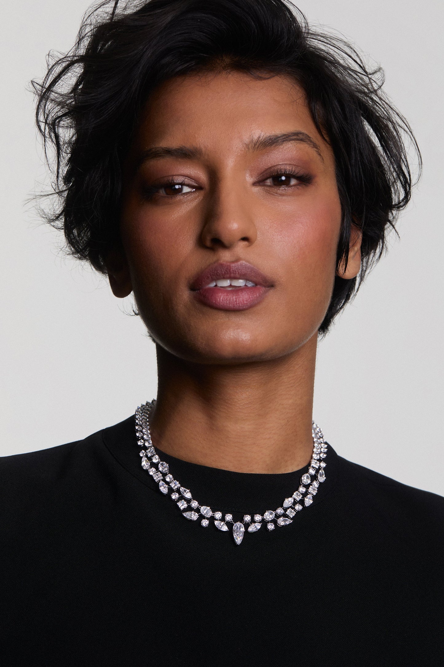 A MODEL LOOKING AT THE CAMERA WEARING A RIVIERA COLLAR NECKLACE AND A BLACK TOP