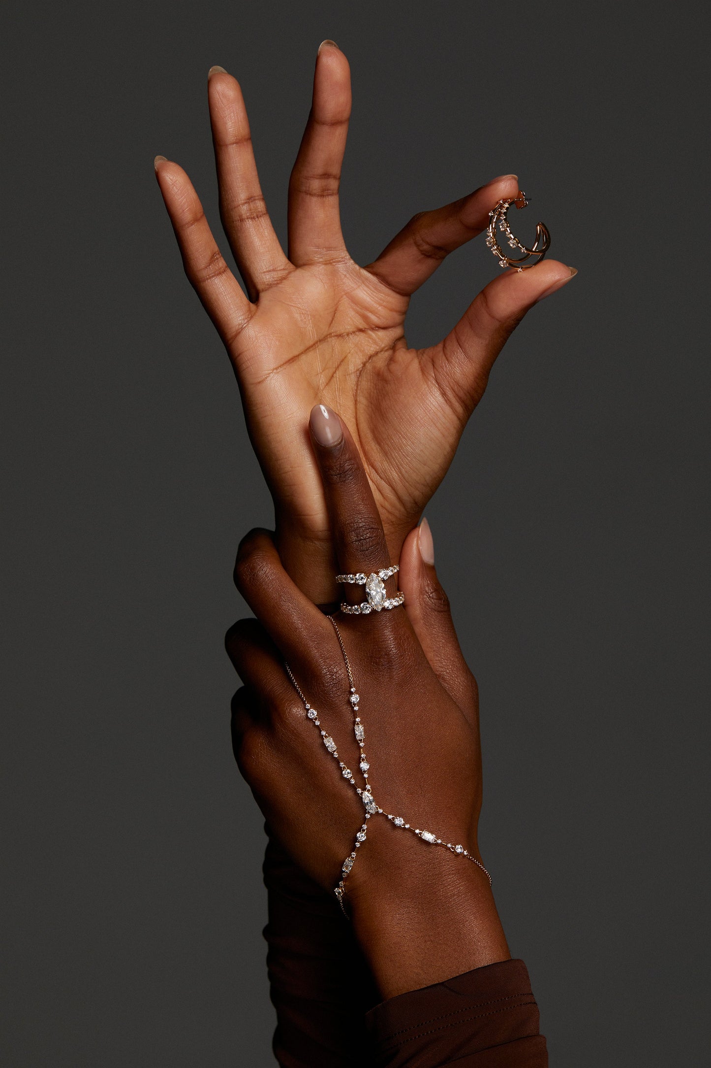 MODEL WEARING EVERLEIGH HAND CHAIN BRACELET. IT IS A CLOSE UP IMAGE OF JUST HER HAND AND SHE IS HOLDING  HOOP EARRRING WITH THE OTHER HAND. 