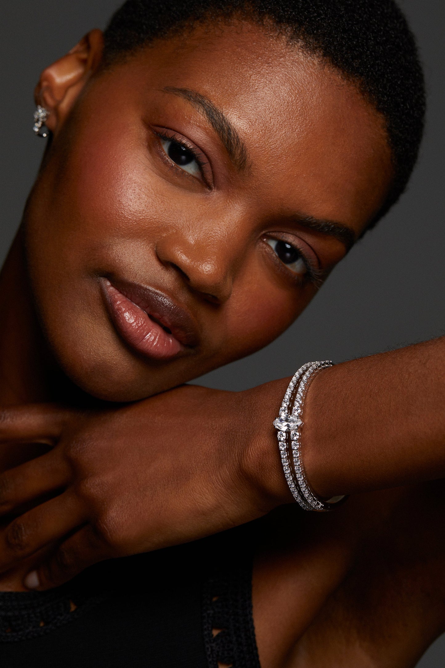 MODEL WEARING EVERLEIGH HINGE BRACELET. SHE IS LOOKING DIRECTLY INTO THE CAMERA WITH HER WRIST AGAINST HER CHIN SO THAT THE BRACELET IS IN FULL VIEW. SHE IS WEARING A BLACK CROCHET TOP. 