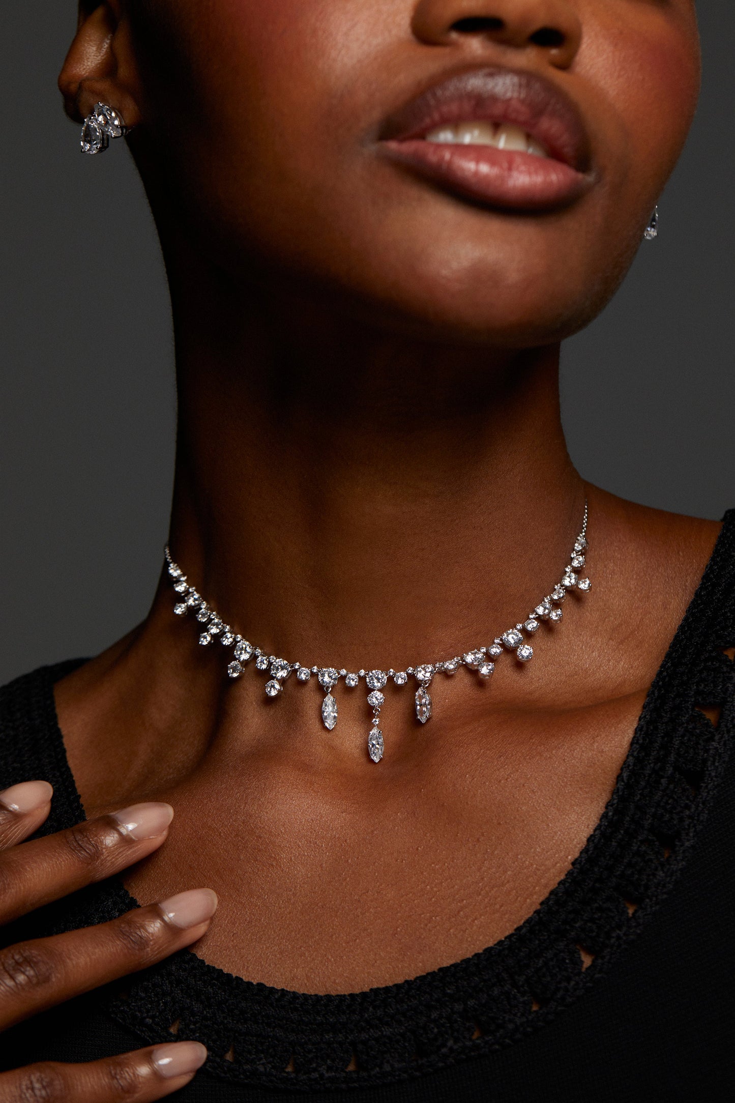 CLOSE UP IMAGE OF MODEL WEARING EVERLEIGH FRONTAL NECKLACE. IT IS A TIGHT SHOT OF HER NECKLINE. SHE HAS A BLACK CROCHET TOP ON AND ALSO WEARING STUD CZ EARRINGS. 