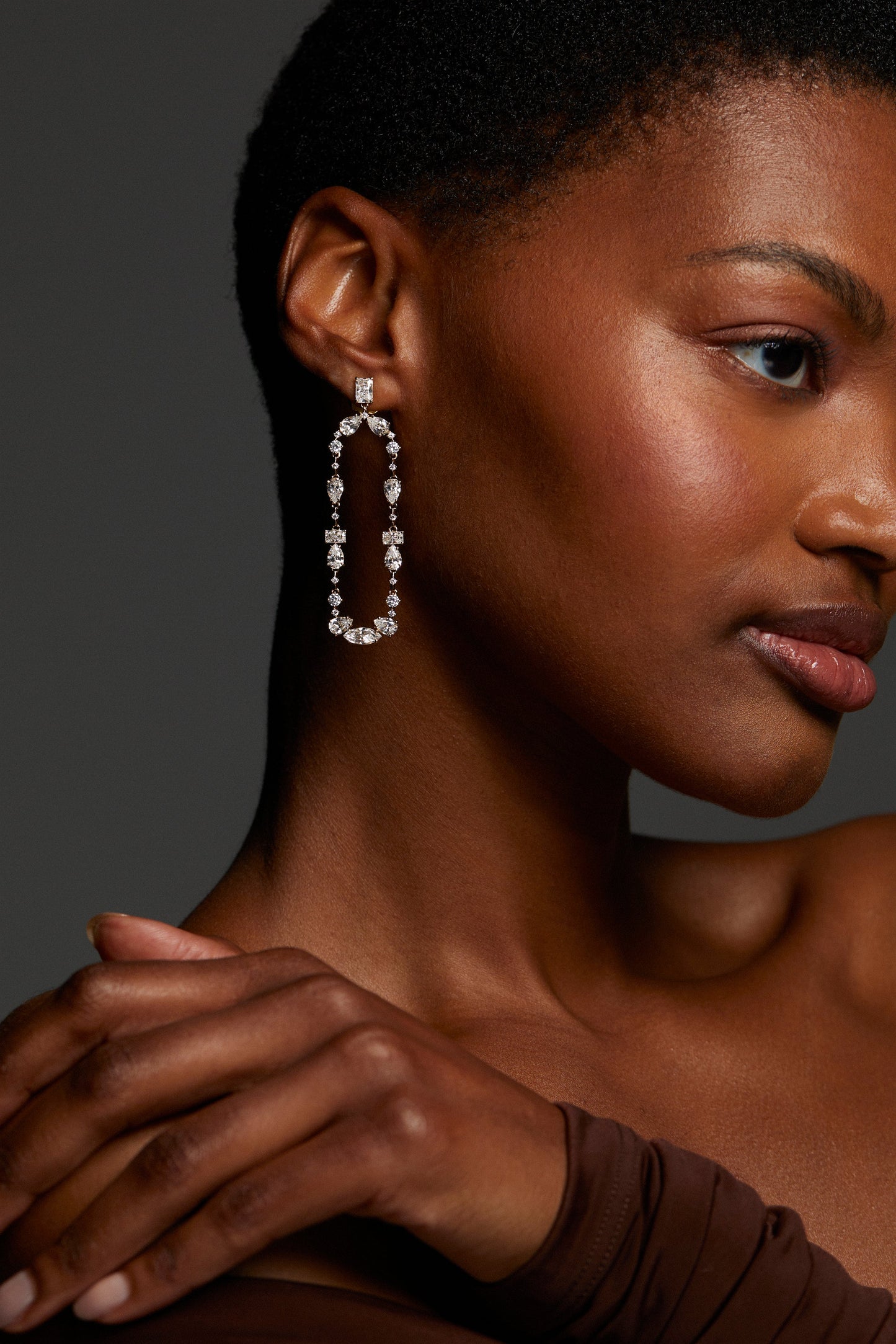 MODEL WEARING EVERLEIGH FRONTAL SWING EARRINGS. IT IS A CLOSE UP IMAGE OF HER PROFILE. HER HAND IS ON HER SHOULDER SHE HAS ON A BROWN LONG SLEEVE OFF THE SHOULDER TOP. 