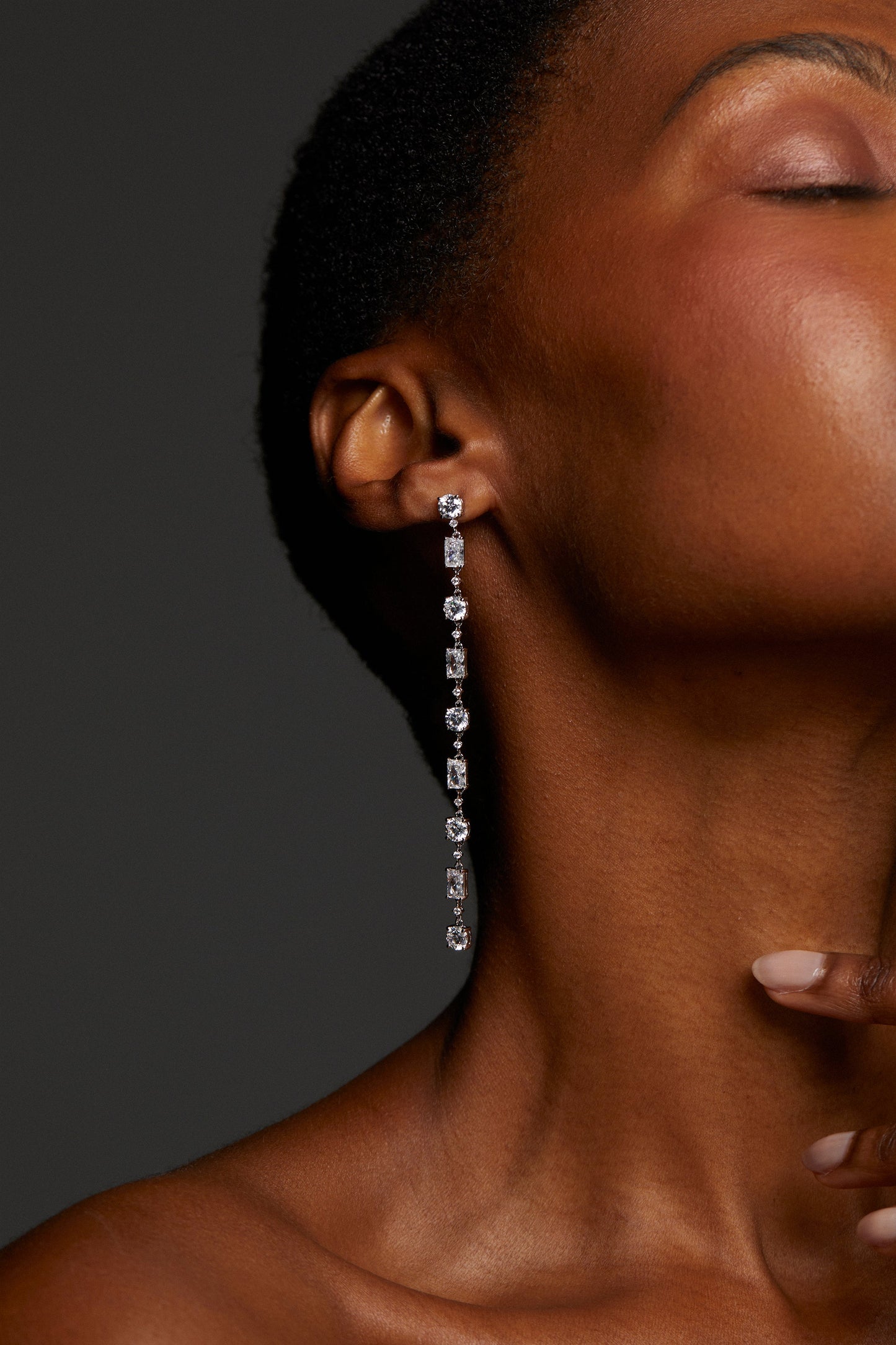 MODEL WEARING EVERLEIGH LONG LINEAR EARRINGS. IT IS A CLOSE UP IMAGE WITH HALF HER FACE CROPPED. SHE HAS A BUZZ CUT SO THAT THE EARRINGS ARE IN FULL VIEW. 