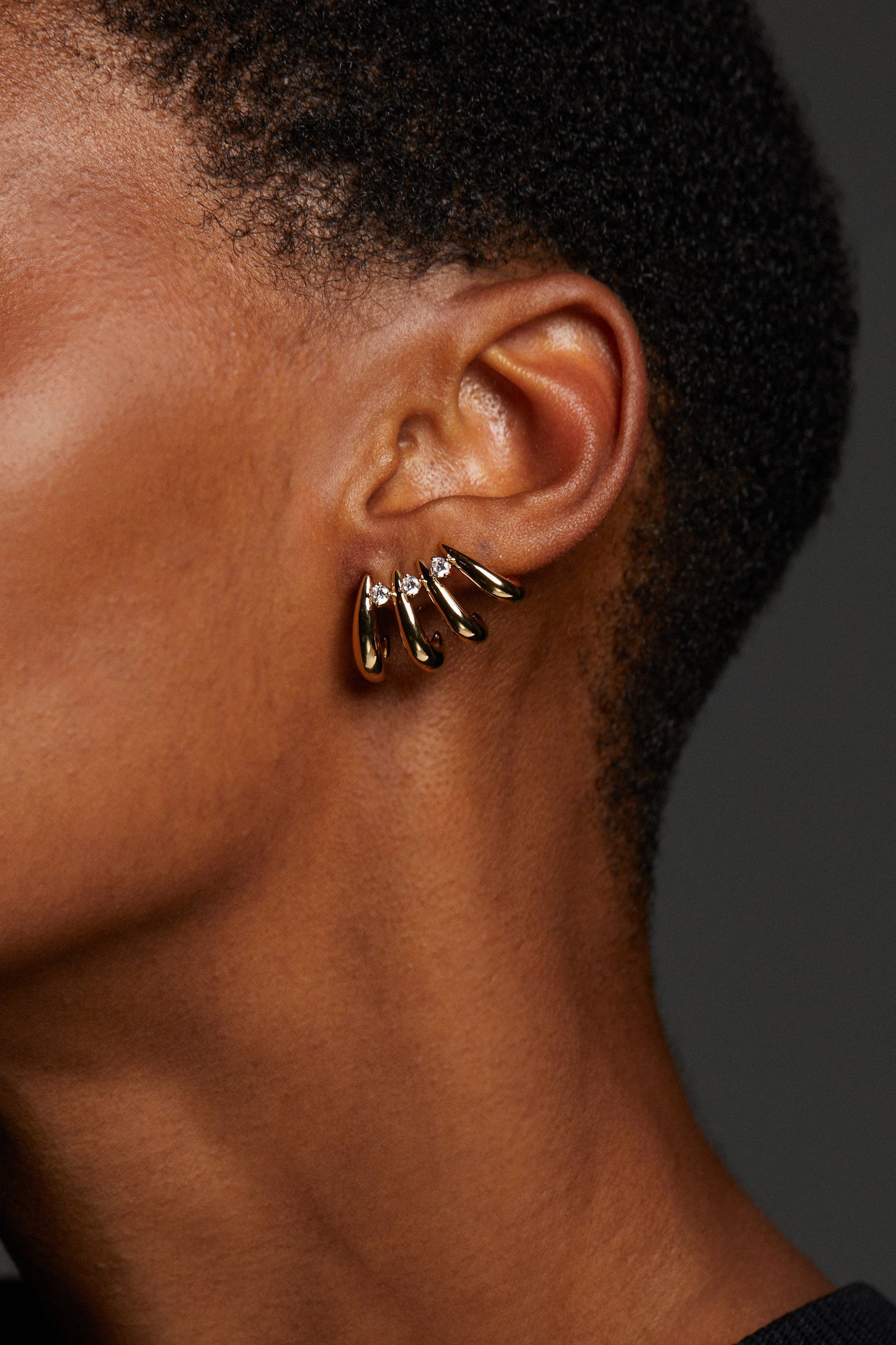 CLOSE UP IMAGE OF MODEL WEARING PISA MULTI HOOP CLIMBER EARRINGS. SHE HAS A BUZZED HAIR CUT AND IT IS A DETAIL SIDE VIEW OF HER EAR AND THE EARRINGS. 