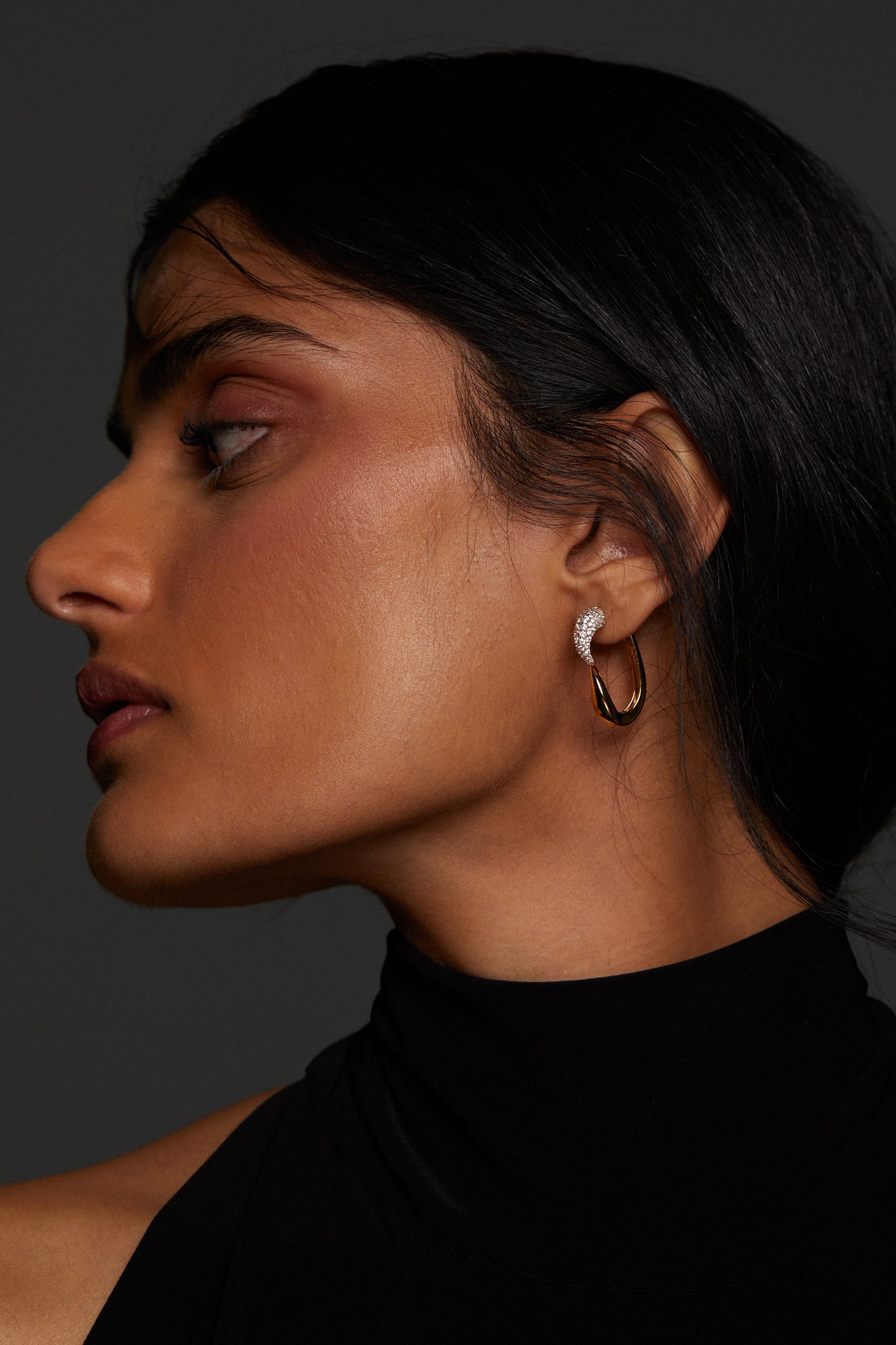 MODEL WEARING PISA FRONTBACK EARRINGS. IT IS A PROFILE IMAGE WITH HER HAIR TUCKED BEHIND HER EAR AND SHE IS WEARING A BLACK HIGH NECK SLEEVELESS TOP. 
