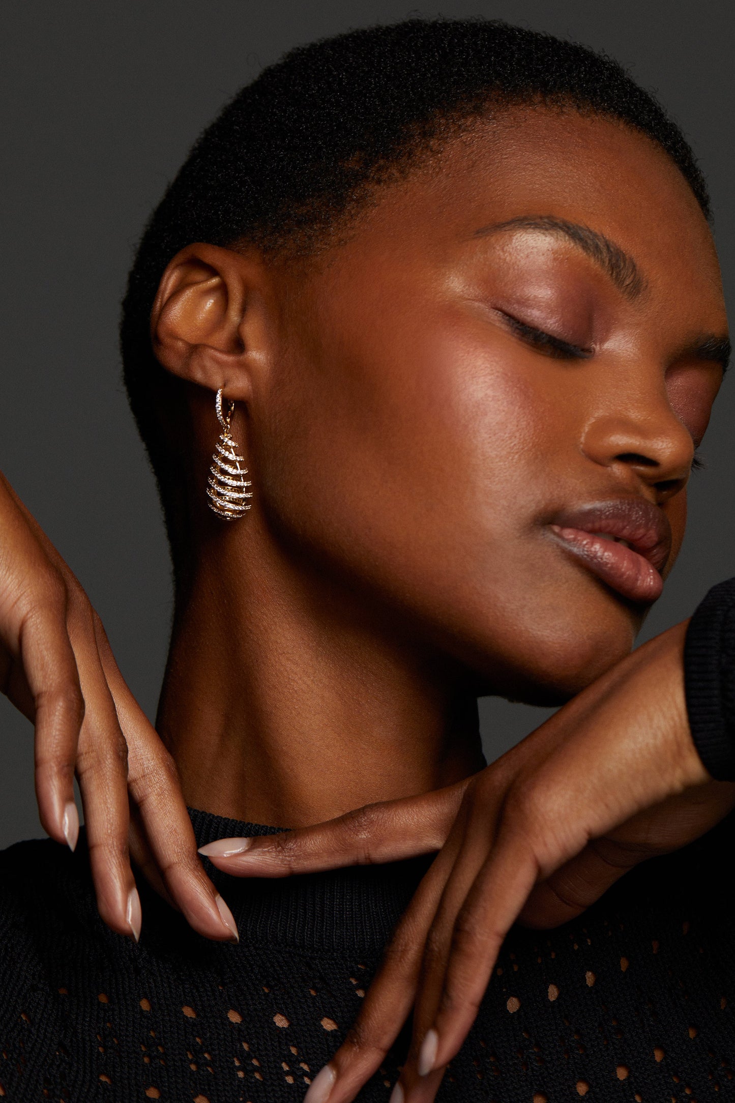 MODEL WEARING PISA OPEN PAVE DROP LEVERBACK. HER EYES ARE CLOSED AND SHE'S HOLDING BOTH HANDS UNDER HER FACE. SHE HAS A BUZZED HAIRCUT AND IS WEARING A BLACK CUTOUT SWEATER.