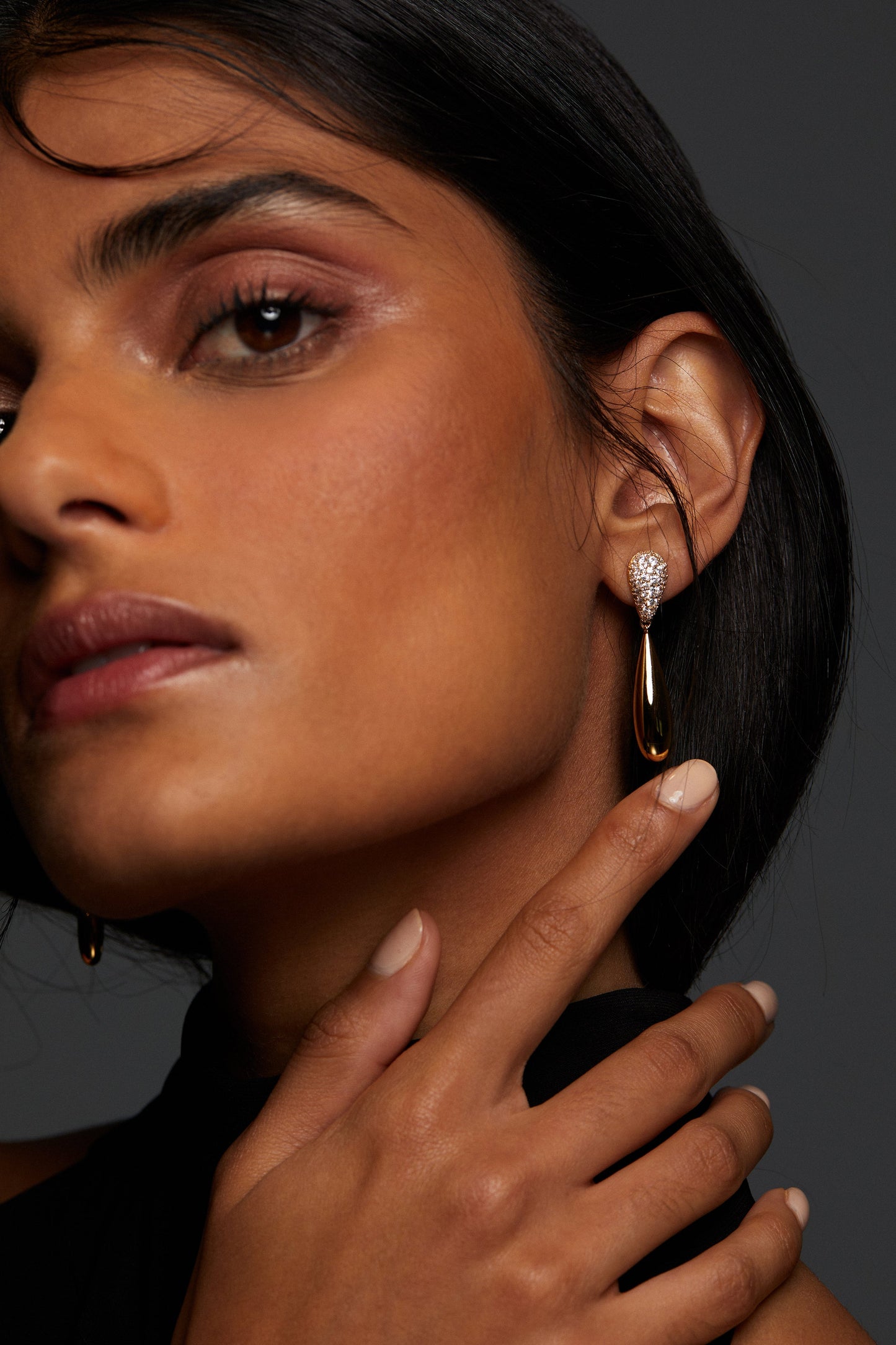 MODEL WEARING PISA LARGE PAVE DROP EARRINGS. HER HAND IS REACHING UP TO HER EAR. HER HAIR IS TIED BACK IN A LOW PONYTAIL. SHE IS WEARING A BLACK TURTLENECK. 
