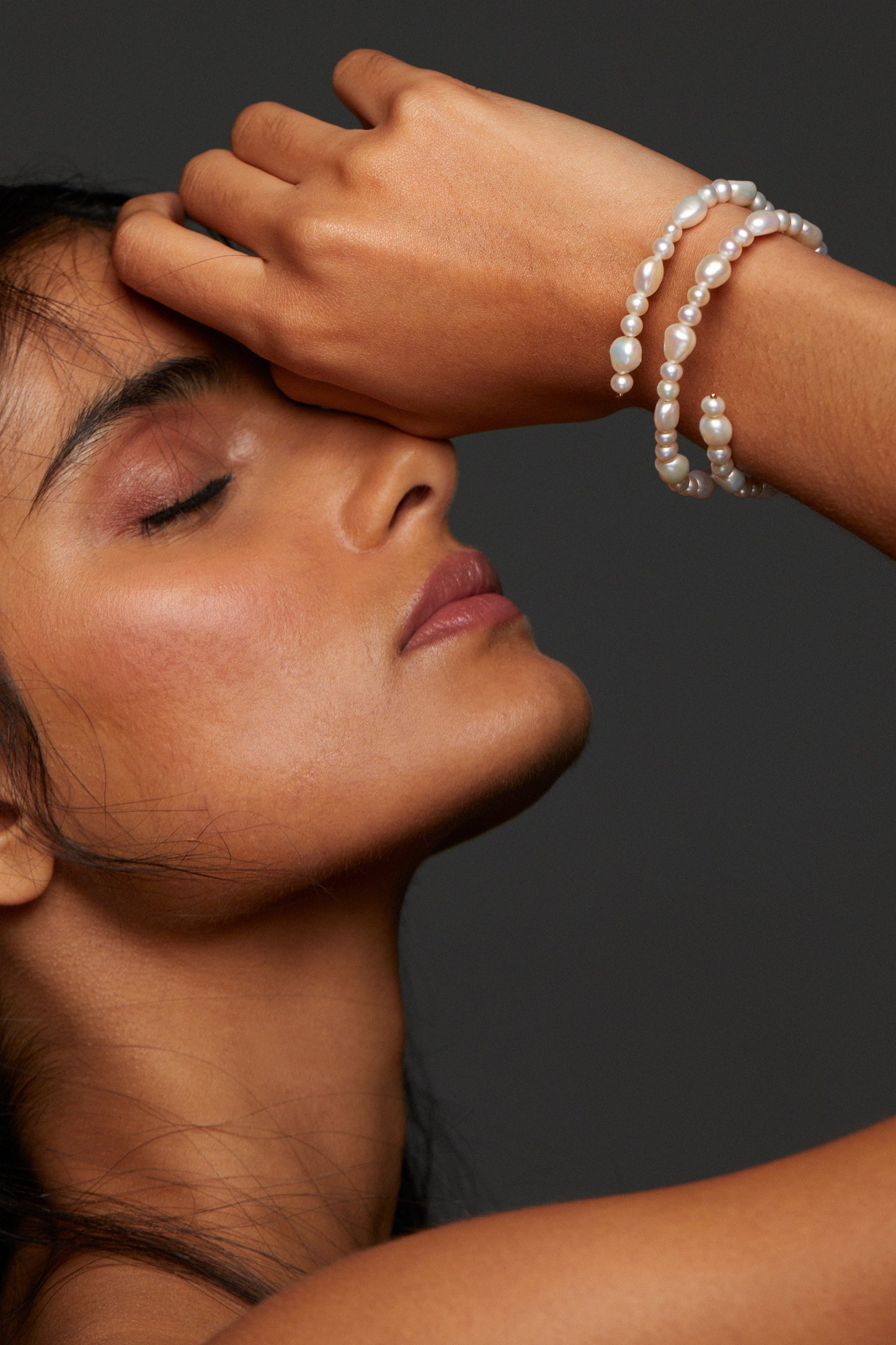 MODEL WEARING POPPY TRIPLE WRAP BRACELET. HER EYES ARE CLOSED WITH HER HAND UP AGAINST HER FACE. 