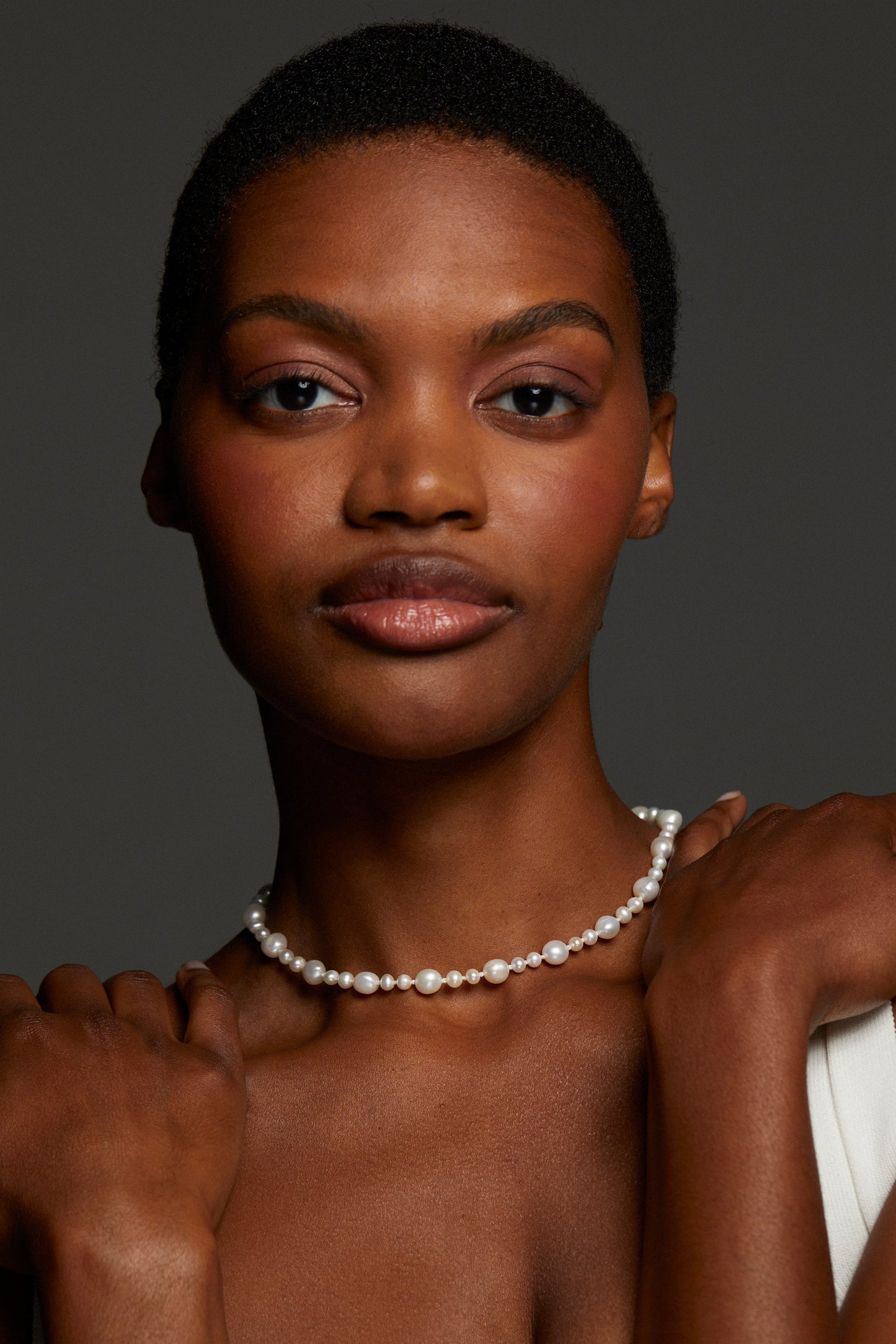 MODEL WEARING POPPY MIXED FRESHWATER PEARL NECKLACE. SHE IS LOOKING DIRECTLY INTO THE CAMERA WITH HER HANDS ON HER SHOULDERS. SHE HAS A BUZZED HAIRCUTE. 