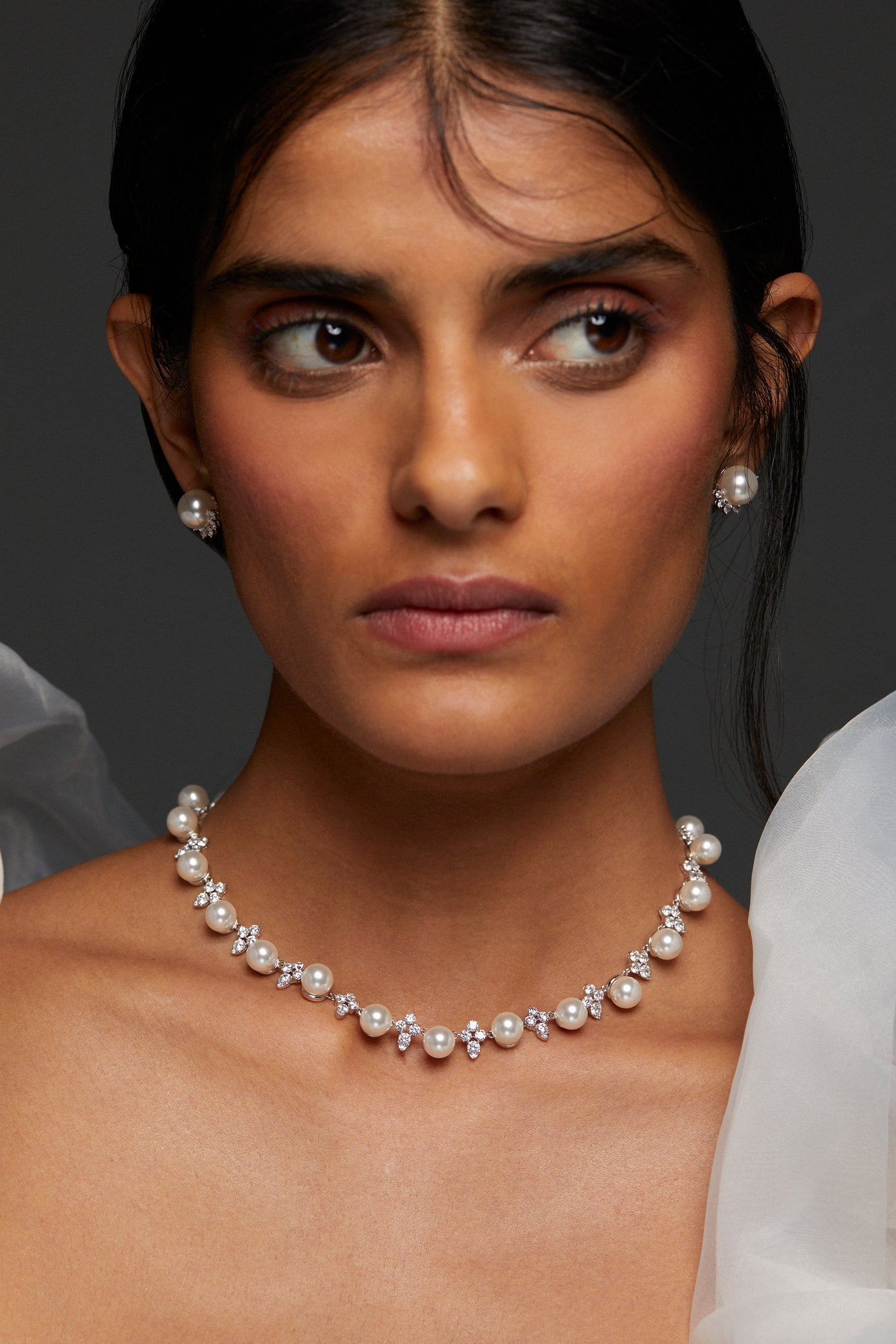 Model WEARING VENUS PEARL CLUSTER COLLAR NECKLACE. HER HAIR IS PULLED BACK IN A BUN AND SHE HAS ON PEARL STUD EARRINGS ON FROM THE VENUS COLLECTION TOO. SHE IS LOOKING TO THE SIDE OF THE FRAME OF THE IMAGE. 