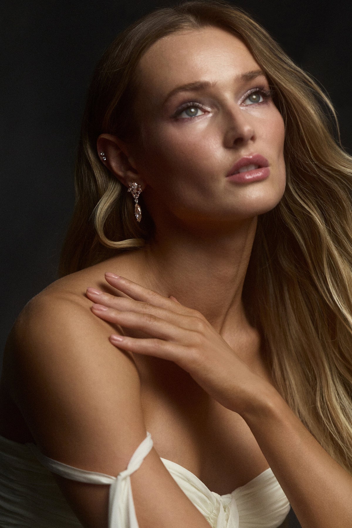A MODEL LOOKING UPWARD WITH HER HAND RAISED TO HER SHOULDER, AS SHE WEARS THE CANNES DROP EARRINGS