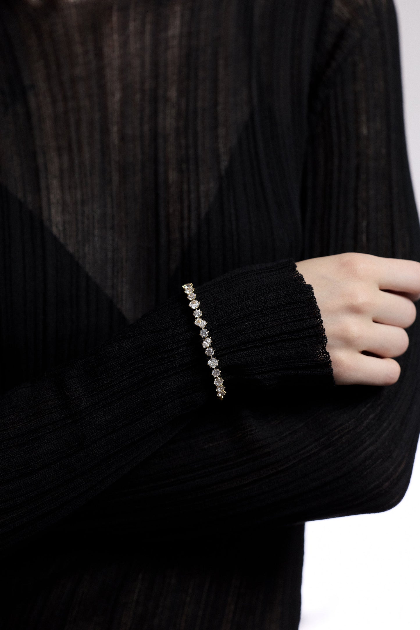 CLOSE UP OF A MODEL’S WRIST WITH HER ARMS FOLDED IN FRONT OF HER, AS SHE WEARS A SHEER BLACK DRESS AND THE CELINE MULTI CZ HINGE BRACELET
