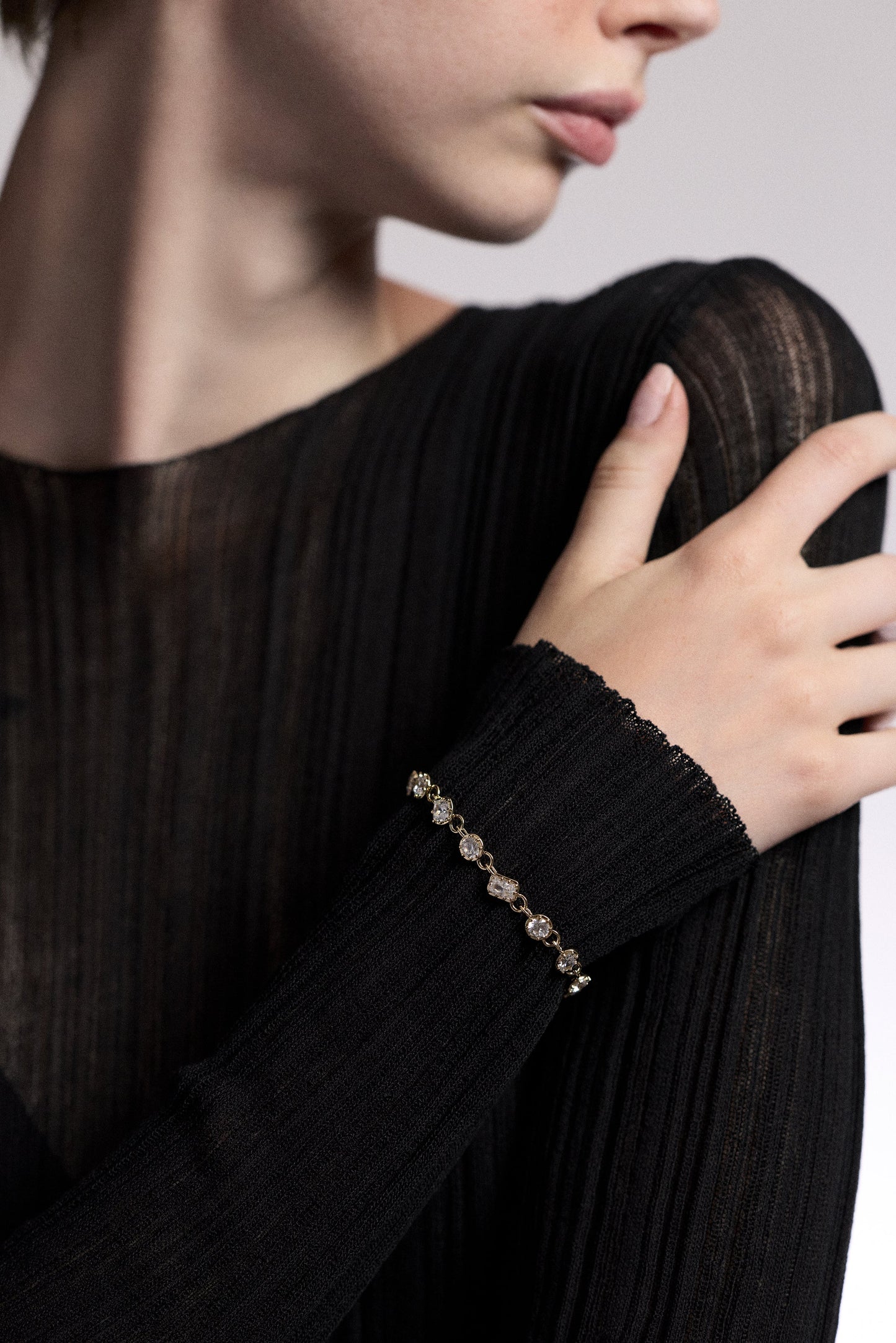 CLOSE UP OF A MODEL’S WRIST RESTING AGAINST HER SHOULDER, AS SHE WEARS A SHEER BLACK DRESS AND THE CELINE MULTI CZ LINE BRACELET