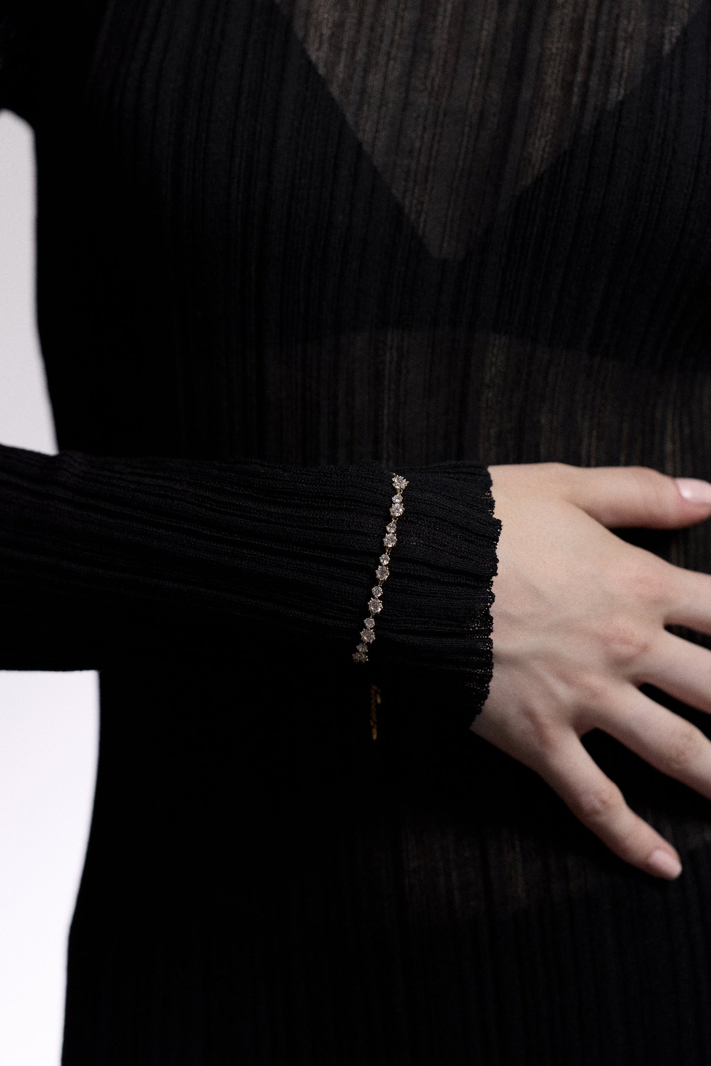 CLOSE UP OF A MODEL’S WRIST WITH HER HAND RESTING AGAINST HER TOSRO, AS SHE WEARS A SHEER BLACK DRESS AND THE CELINE ADJUSTABLE BOLO BRACELET