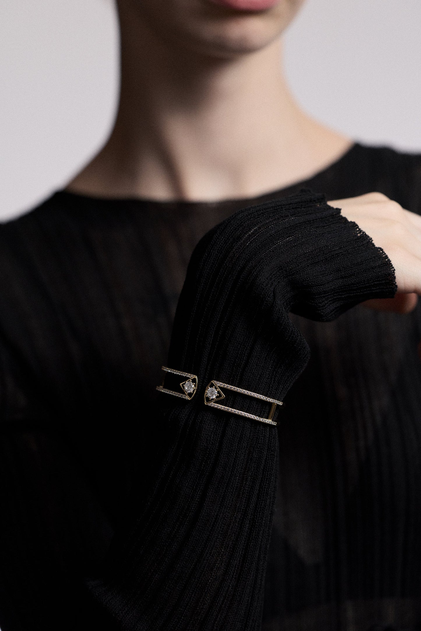 CLOSE UP OF A MODEL’S WRIST LIFTED IN FRONT OF HER, AS SHE WEARS A SHEER BLACK DRESS AND THE CELINE WIDE HINGE BRACELET LAYERED OVER THE SLEEVE