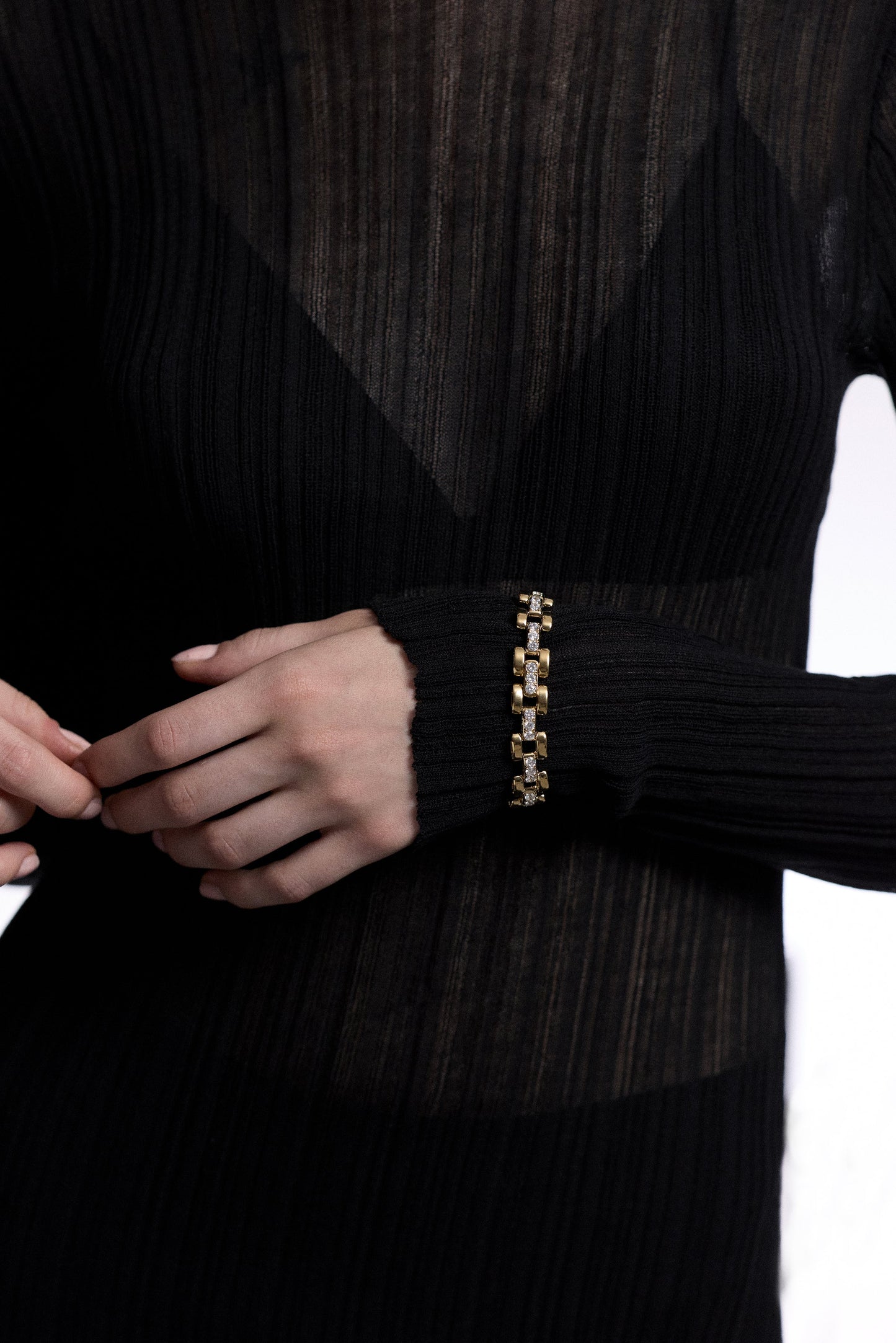 A CLOSE UP OF A MODEL’S TORSO WITH HER HAND ACROSS HER STOMACH, AS SHE WEARS A SHEER BLACK DRESS AND THE CELINE WATCH CHAIN BRACELET