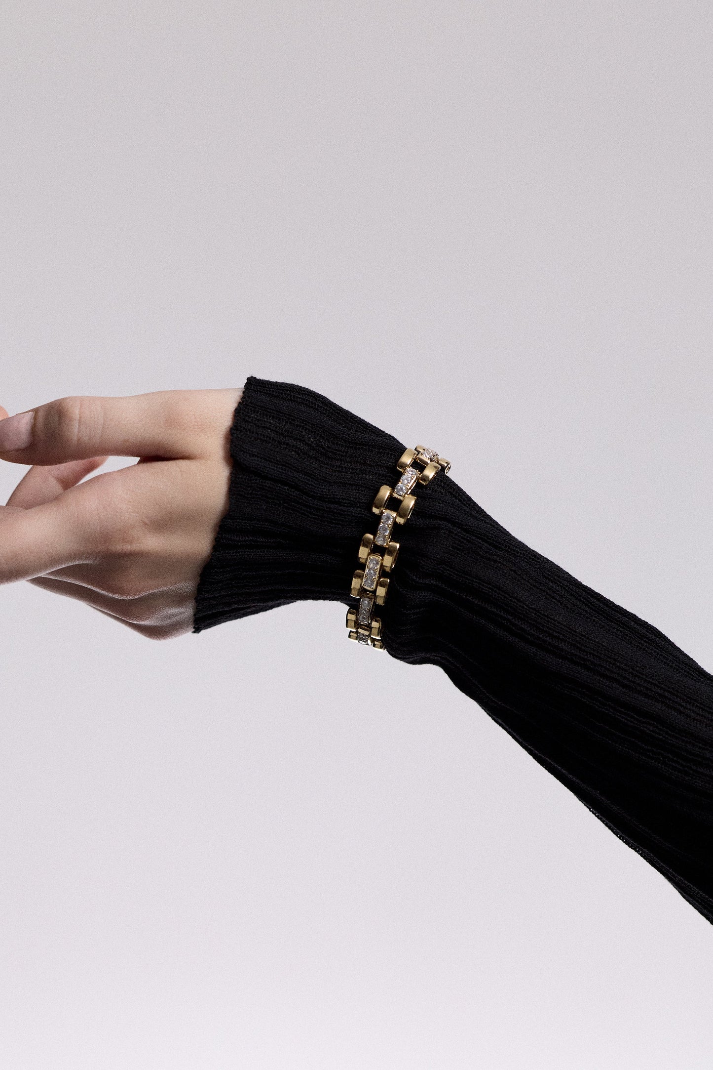AN ARM AND WRIST OUTSTRETCHED, WEARING A SHEER BLACK SLEEVE AND THE CELINE WATCH CHAIN BRACELET LAYERED OVER IT