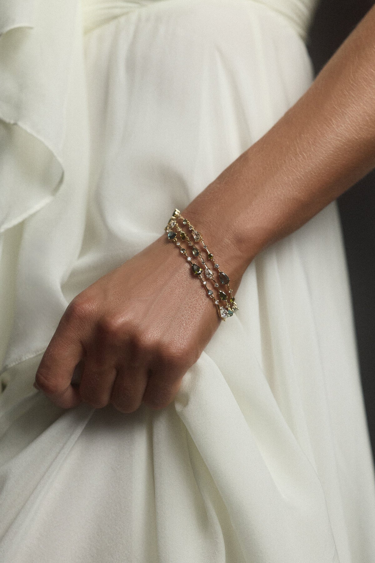 CLOSE UP OF A MODEL’S ARM HOLDING HER WHITE DRESS AND WEARING THE HERA MULTI 3 LAYER LINE BRACELET