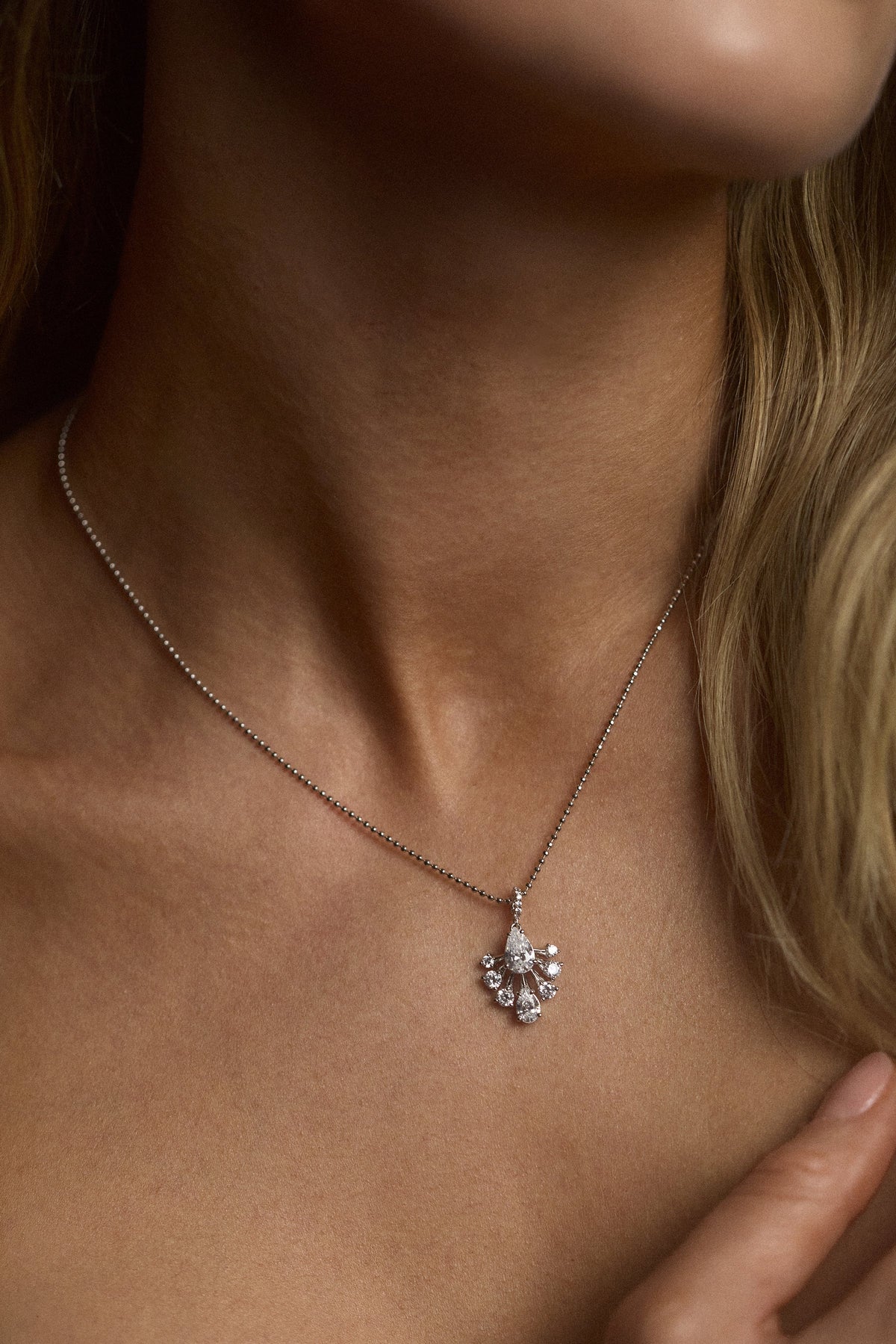 CLOSE UP OF A MODEL’S NECK WITH HER BLONDE HAIR IN FRAME WEARING THE HERA FAN PENDANT NECKLACE