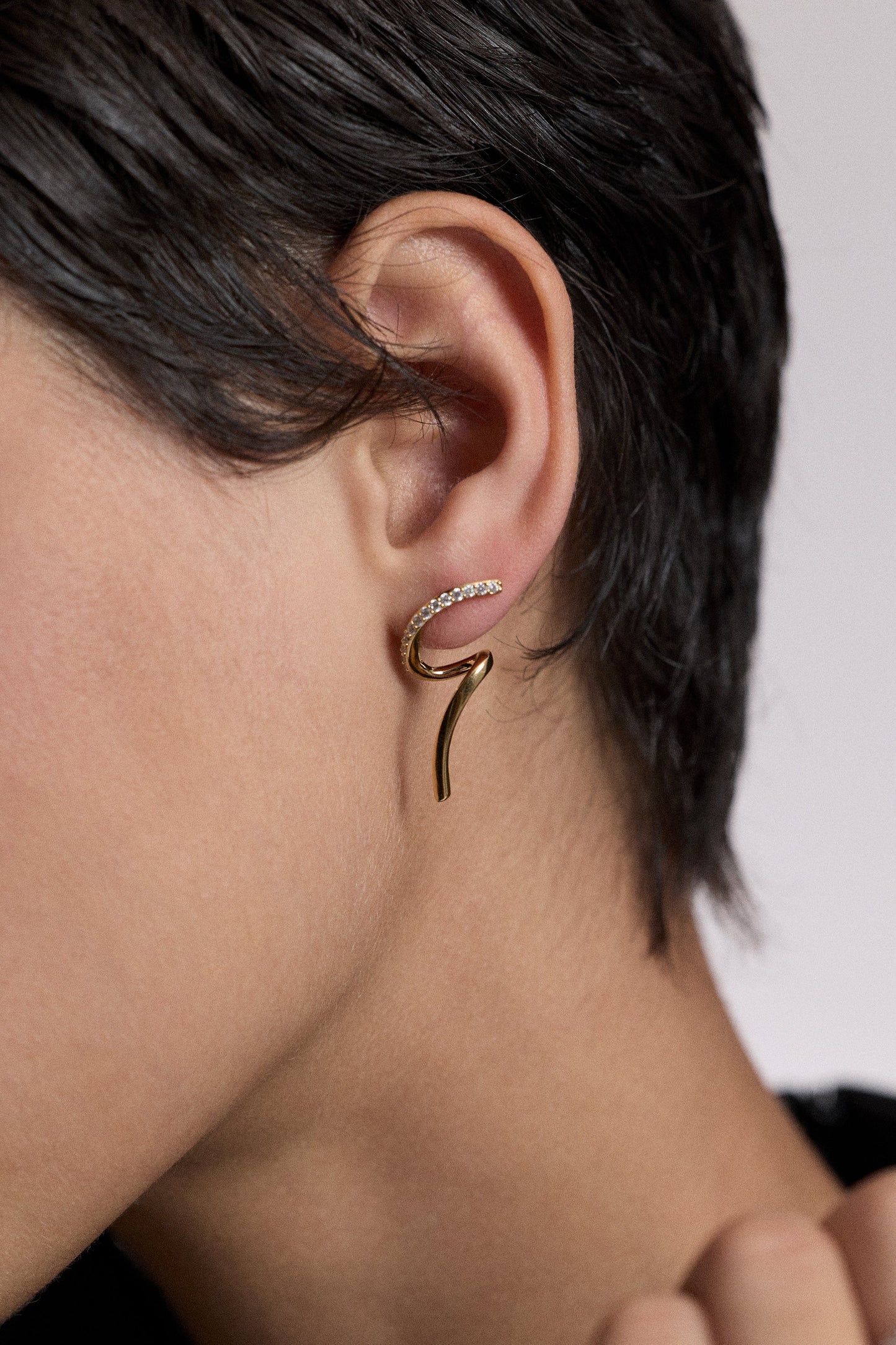 CLOSE UP OF A MODEL’S EAR WITH SHORT BLACK HAIR WEARING THE MUSE TWIRL STUD EARRINGS