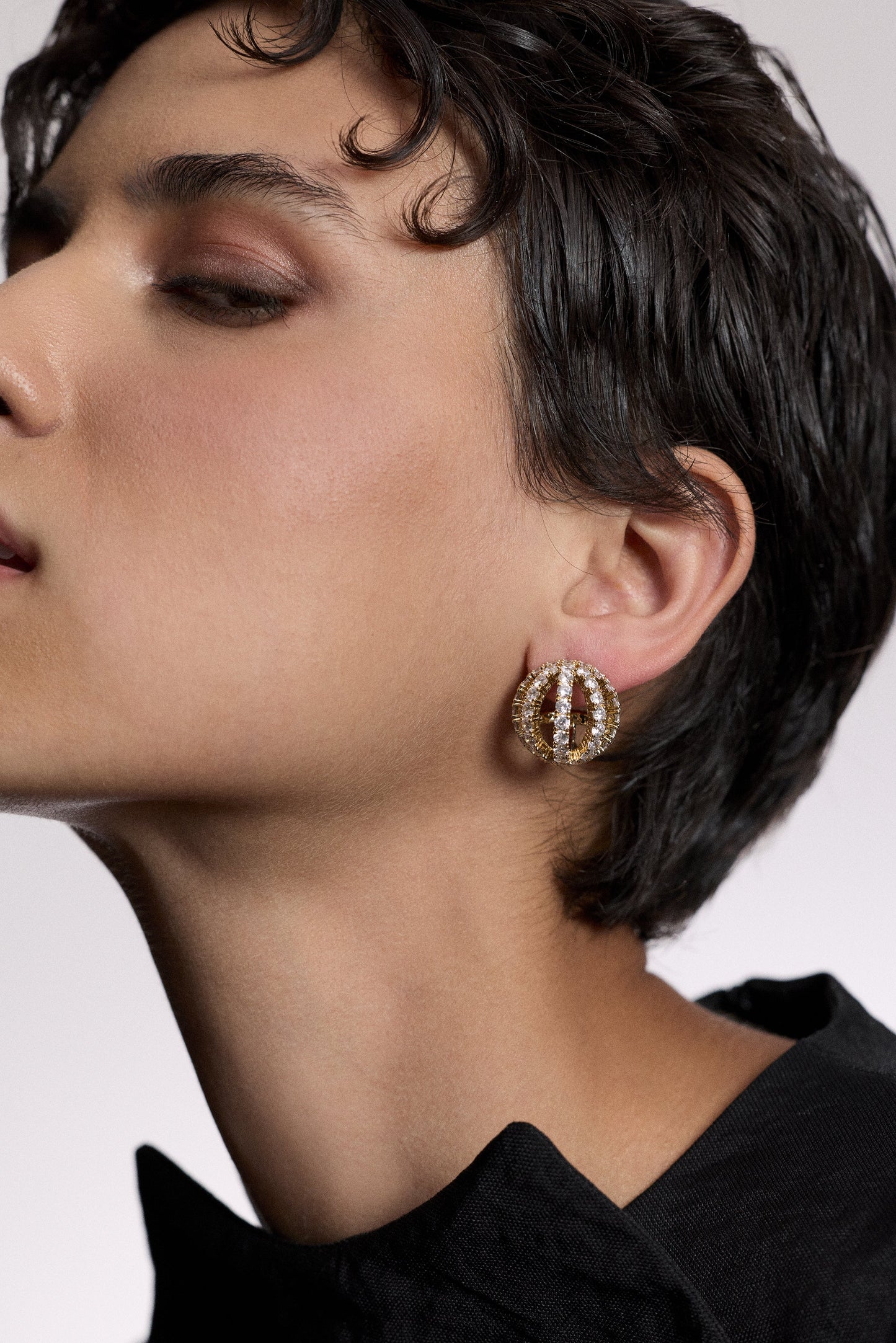 CLOSE UP OF A MODEL’S SIDE PROFILE AS SHE WEARS A BLACK TOP AND THE MUSE SPHERE BUTTON EARRINGS