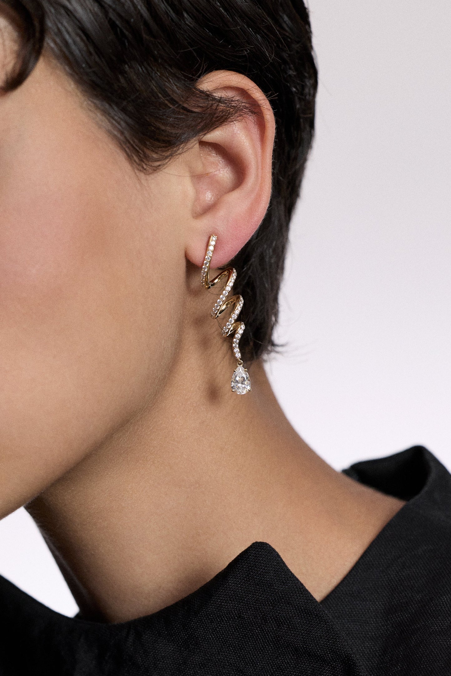 CLOSE UP OF A MODEL’S EAR WITH SHORT BLACK HAIR WEARING THE MUSE TWIRL LINEAR DROP EARRINGS
