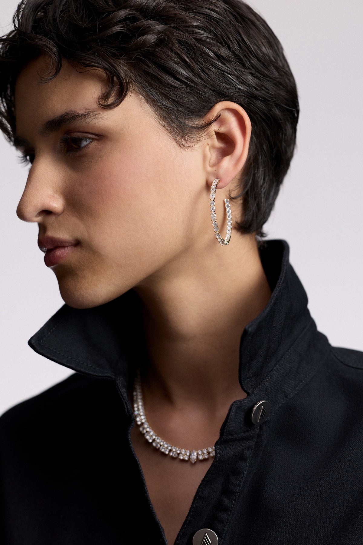 SIDE PROFILE OF A MODEL WITH SHORT BLACK HAIR AND A POPPED COLLAR, AS SHE WEARS THE TWINNIE C HOOP EARRINGS AND TWINNIE STATEMENT COLLAR NECKLACE