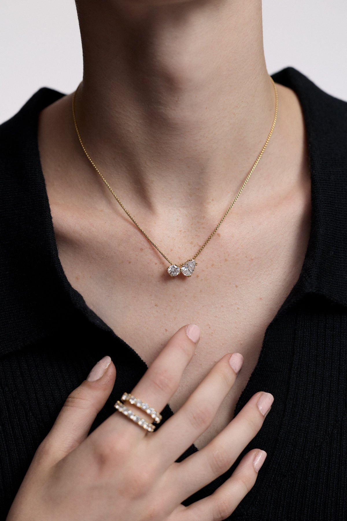 CLOSE UP OF A MODEL’S CHEST WITH HER HAND HELD UP TO HER NECKLINE, AS SHE WEARS A BLACK TOP AND THE TWINNIE TOI MOI PENDANT NECKLACE