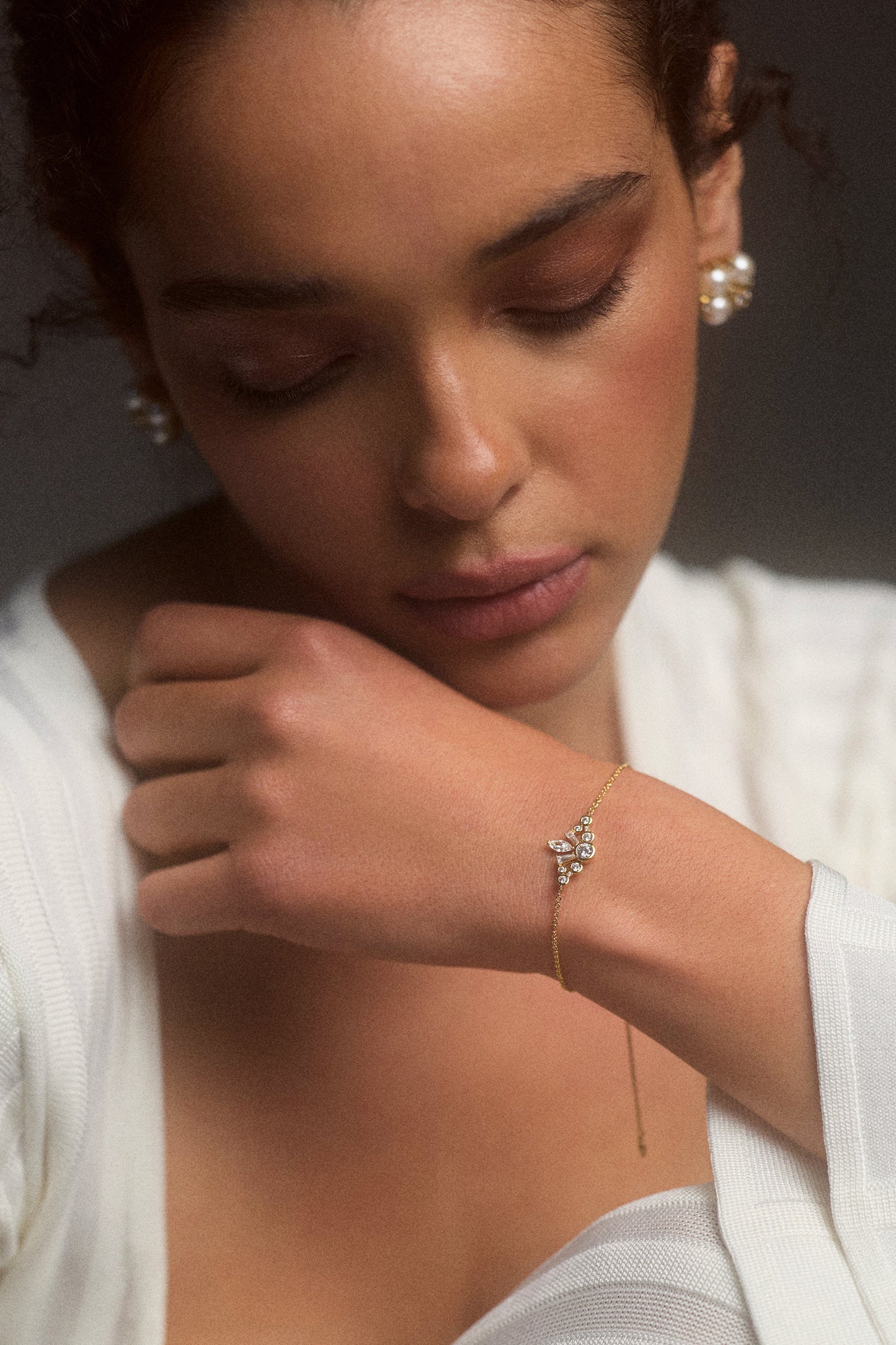 CLOSE UP OF A MODEL LOOKING DOWN WITH HER HAND LIFTED UP TO HER CHIN, WEARING A WHITE DRESS AND THE UNDER THE SEA CROWN BRACELET