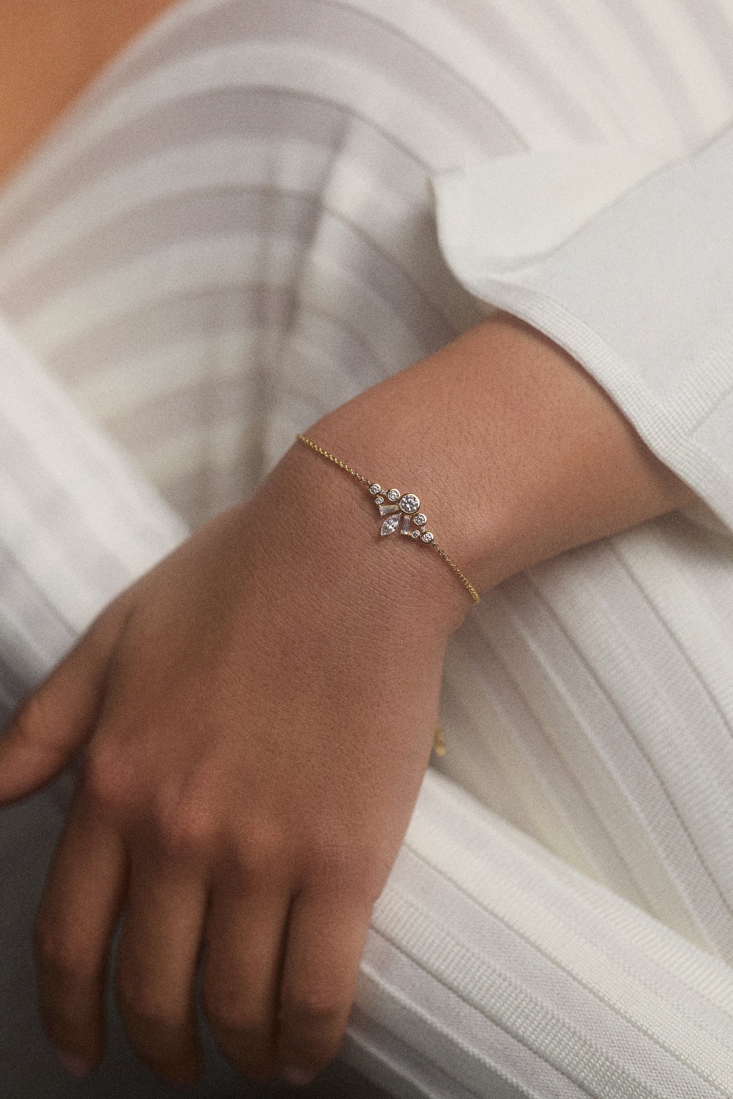 CLOSE UP OF A MODEL’S WRIST RESTING ON HER KNEES AS SHE WEARS A WHITE OUTFIT AND THE UNDER THE SEA CROWN BRACELET