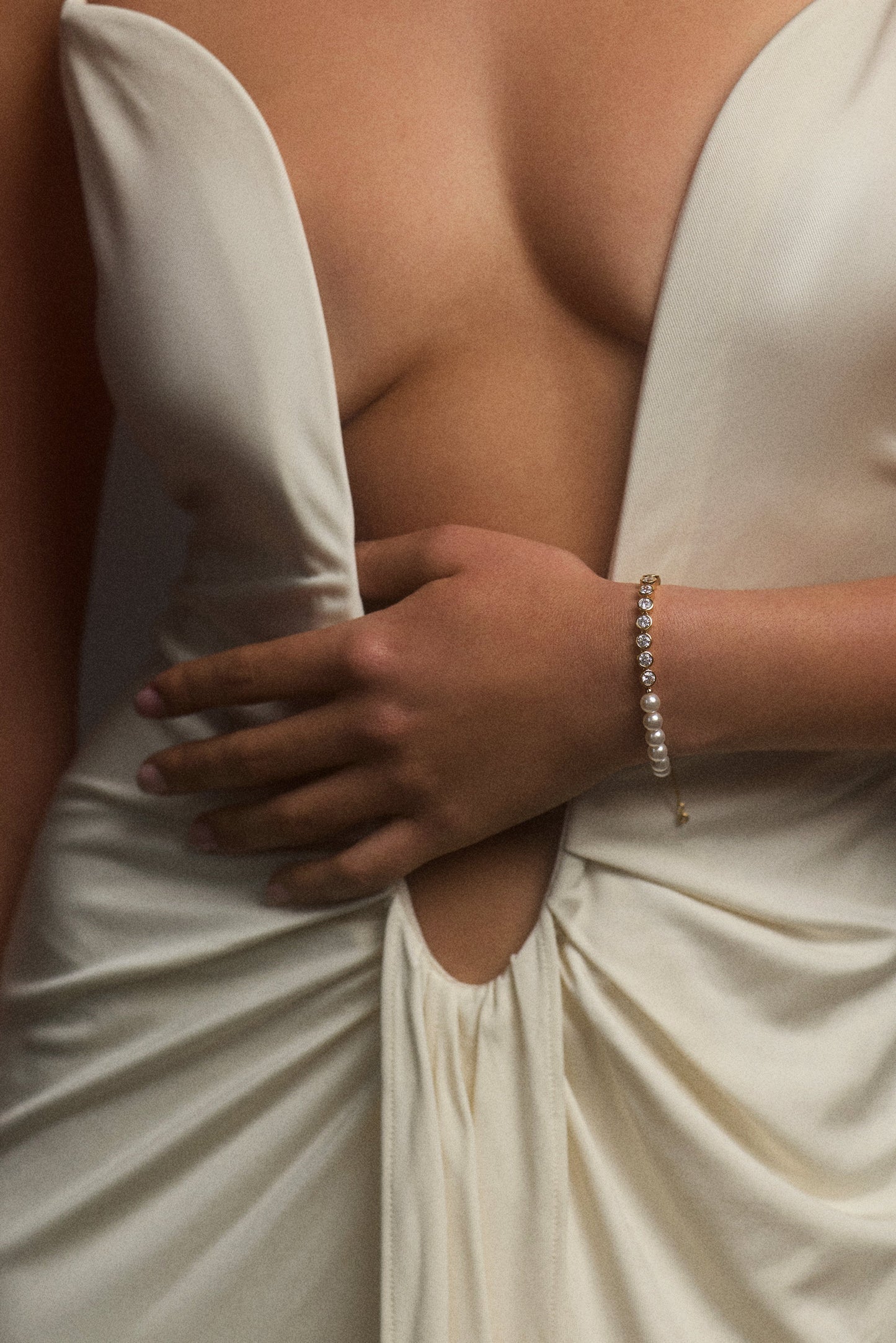 A MODEL’S TORSO IN FRAME, AS SHE WEARS A LOW CUT WHITE DRESS WITH HER HAND ACROSS HER STOMACH, STYLED WITH THE UNDER THE SEA MIXED LINE BRACELET