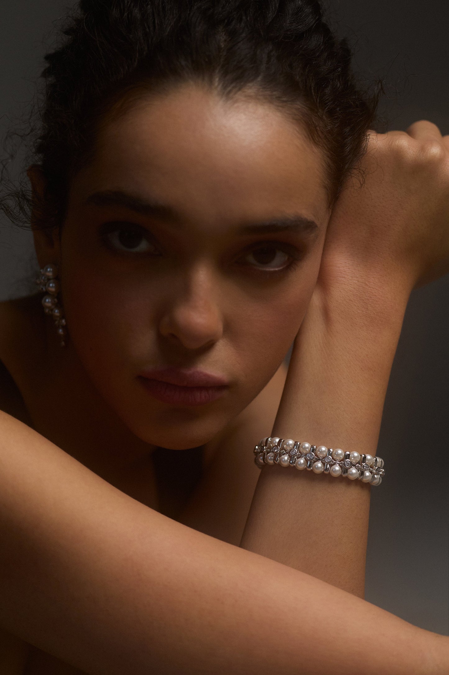 A MODEL LOOKING AT THE CAMERA WITH HER WRIST LIFTED BESIDE HER FACE, WEARING THE UNDER THE SEA RETRO PEARL BRACELET