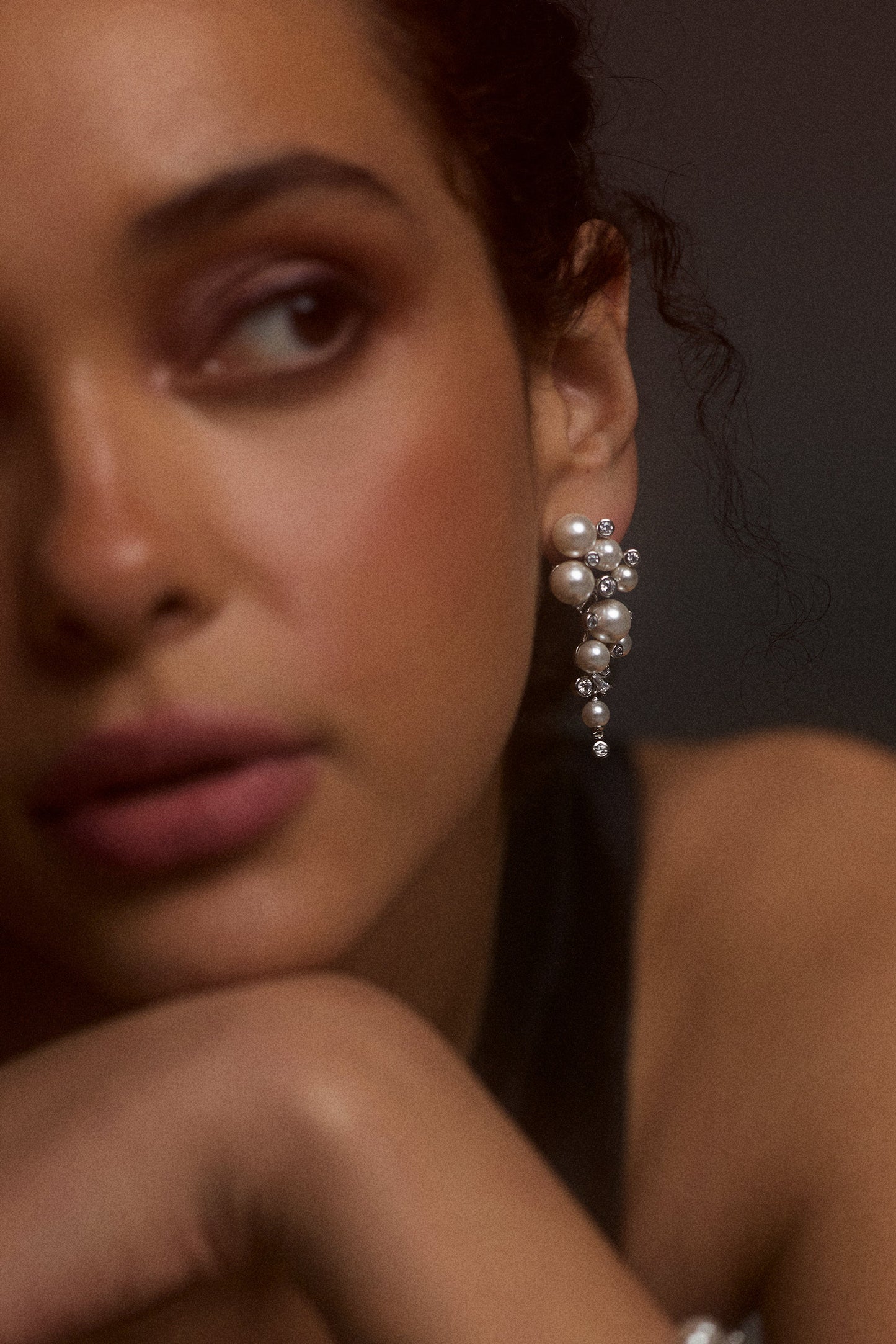 CLOSE UP OF HALF OF A MODEL’S FACE WITH HER HEAD WRESTING ON HER WRIST, WITH HER EAR IN FOCUS WEARING THE UNDER THE SEA CASCADE EARRINGS