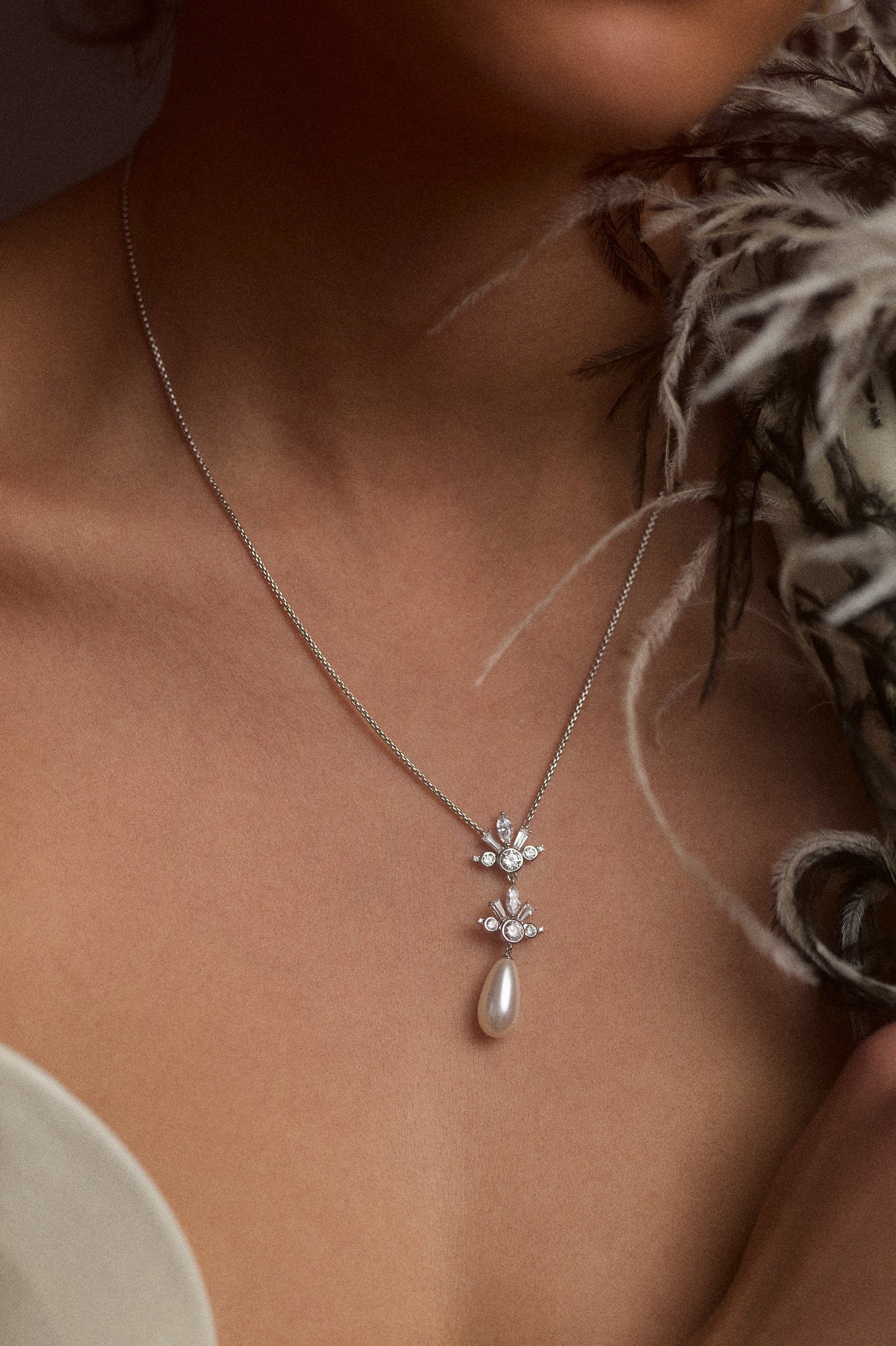 CLOSE UP OF A MODEL’S CHEST WEARING THE UNDER THE SEA TEARDROP PEARL Y NECKLACE, AS A FEATHER JACKET PEAKS OUT FROM THE SIDE