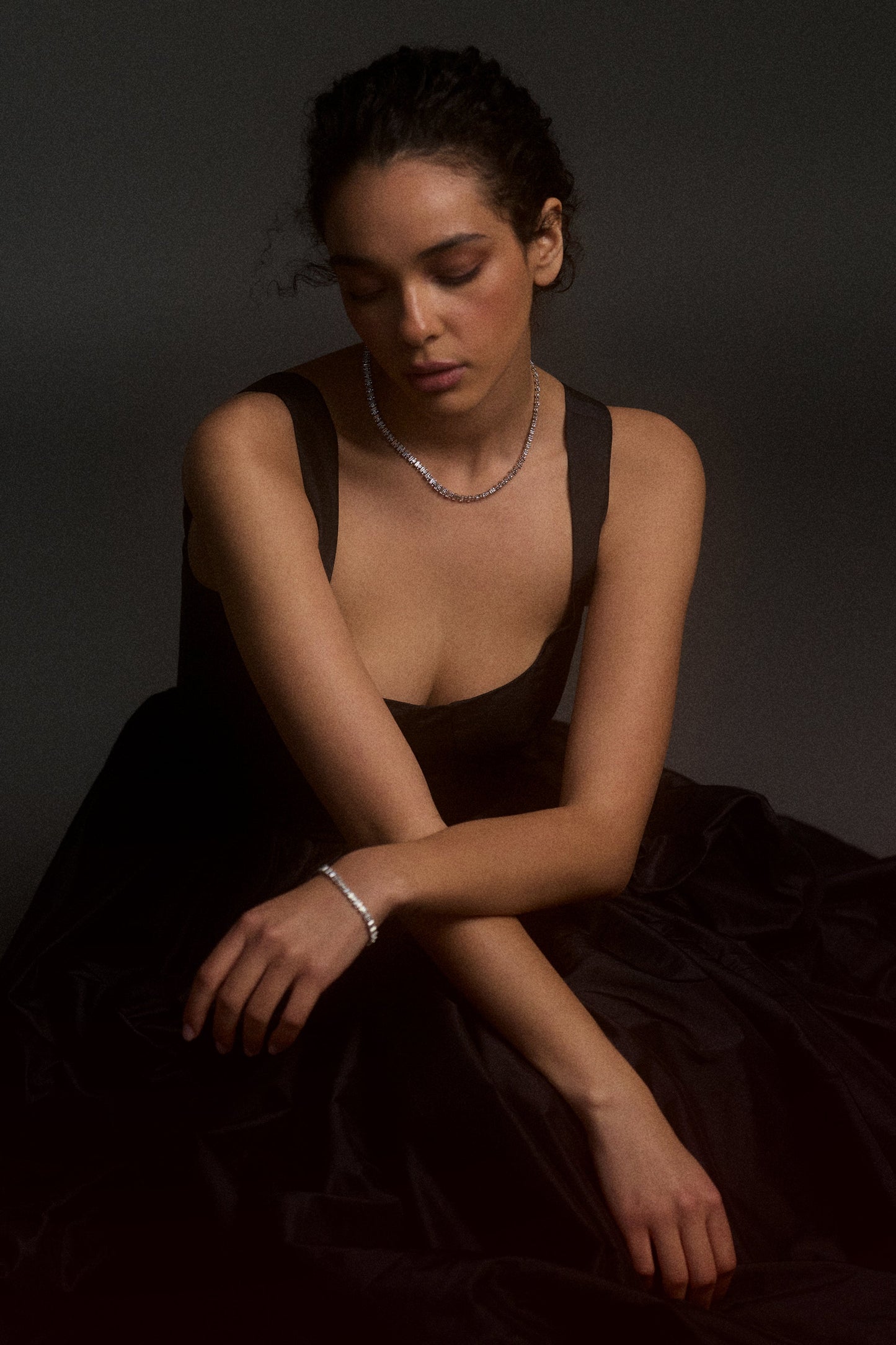 MODEL SQUATTING ON THE FLOOR WITH A BLACK DRESS POOLED AROUND HER, HER ARMS CROSSED AND RESTING ON HER KNEES AS SHE LOOKS DOWN, WEARING THE UNDER THE SEA COLLAR NECKLACE.