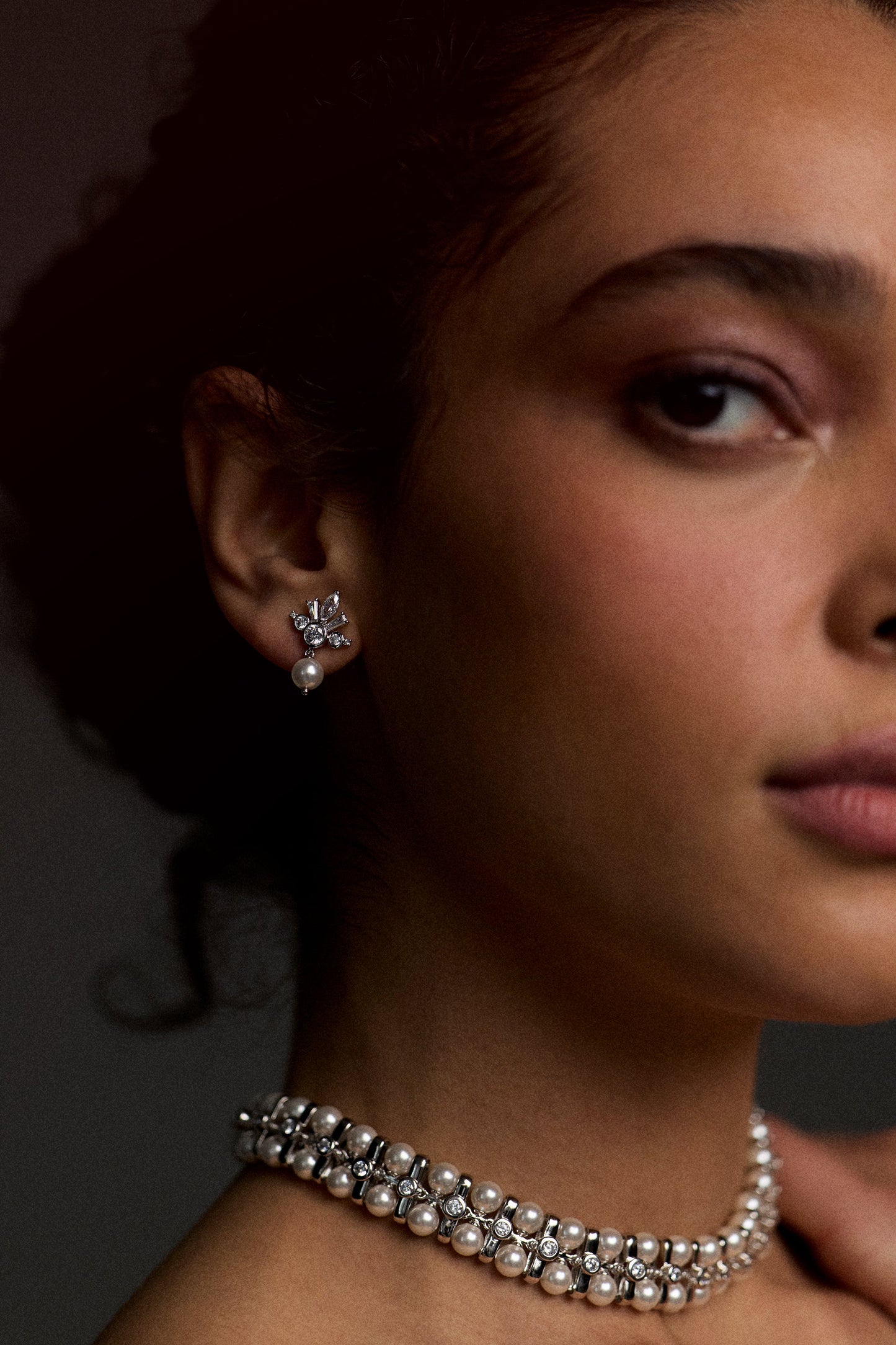 CLOSE UP OF HALF OF A MODEL’S FACE WITH HER NECK AND EAR IN FOCUS, AS SHE WEARS THE UNDER THE SEA RETRO PEARL CHOKER NECKLACE AND THE UNDER THE SEA CROWN PEARL DROP EARRINGS
