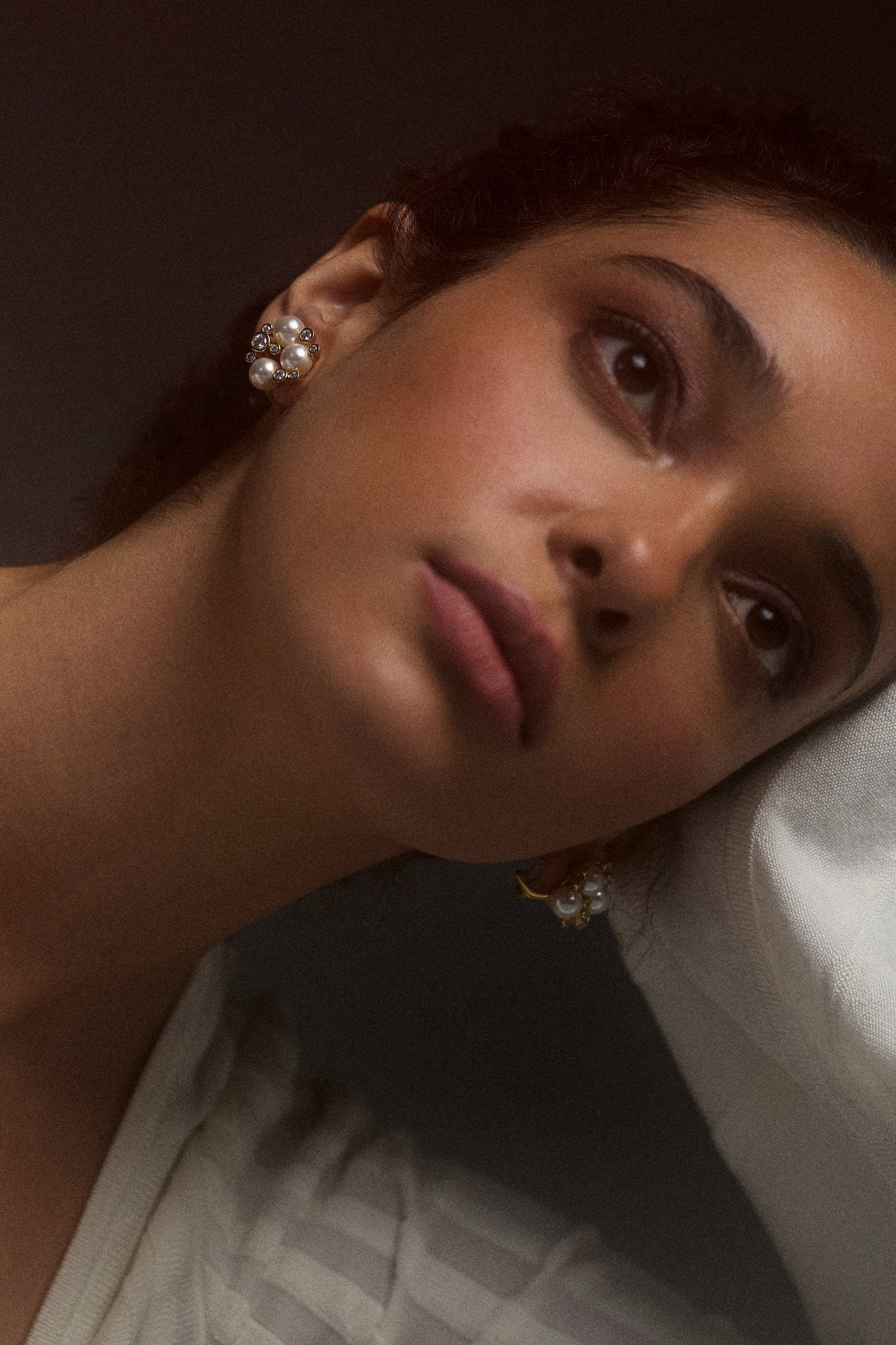 CLOSE UP OF A MODEL'S FACE LEANING ON HER HAND WITH HER HAND RAISED TO THE SIDE OF HER HEAD, WEARING THE UNDER THE SEA CLUSTER STUD EARRINGS
