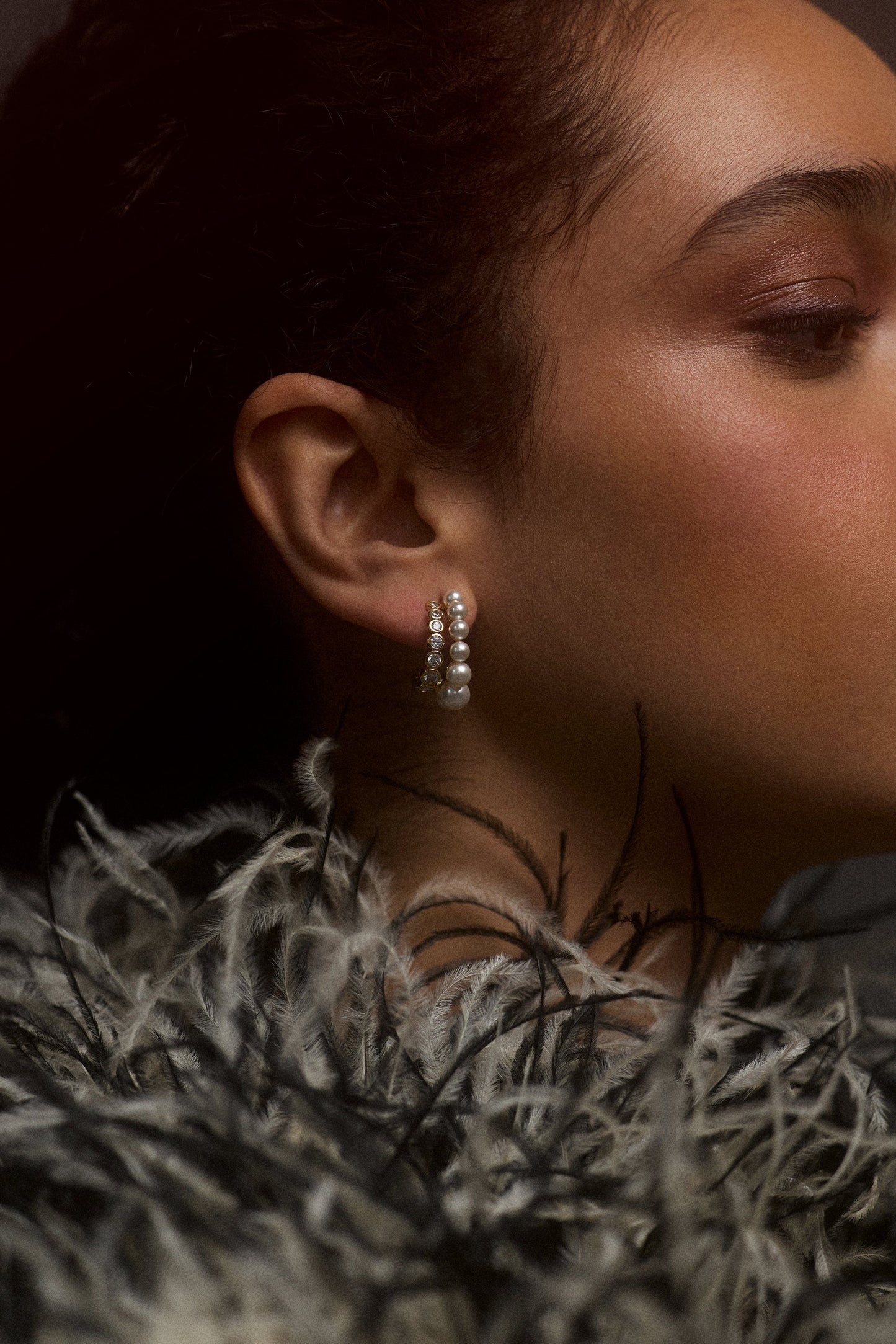CLOSE UP OF THE SIDE PROFILE OF A MODEL AS SHE WEARS A BLCK-AND-WHITE FUR JACKET AND THE UNDER THE SEA DOUBLE ROW J HOOP EARRINGS