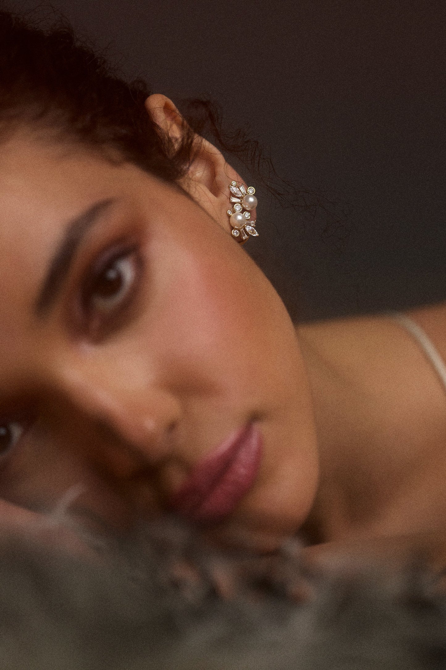 CLOSE UP OF A MODEL’S FACE LAYING DOWN TO THE SIDE, AS SHE WEARS THE UNDER THE SEA CLIMBER STUD EARRINGS