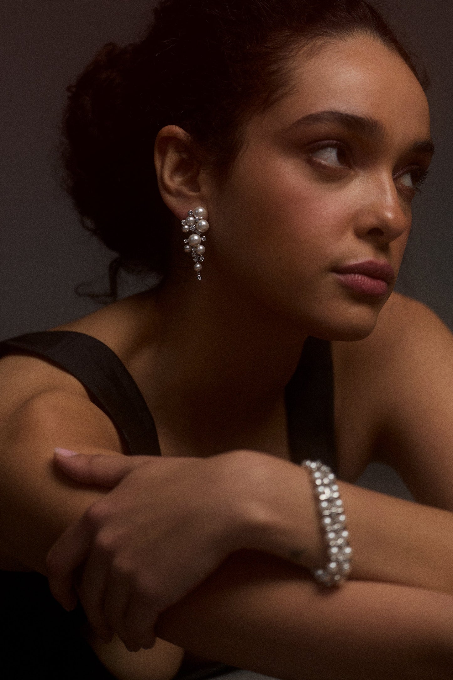 A MODEL LOOKING OFF TO THE SIDE WITH HER ARMS CROSSED IN FRONT OF HER, WEARING A BLACK TOP STYLED WITH THE UNDER THE SEA CASCADE EARRINGS AND THE *BRACELET*